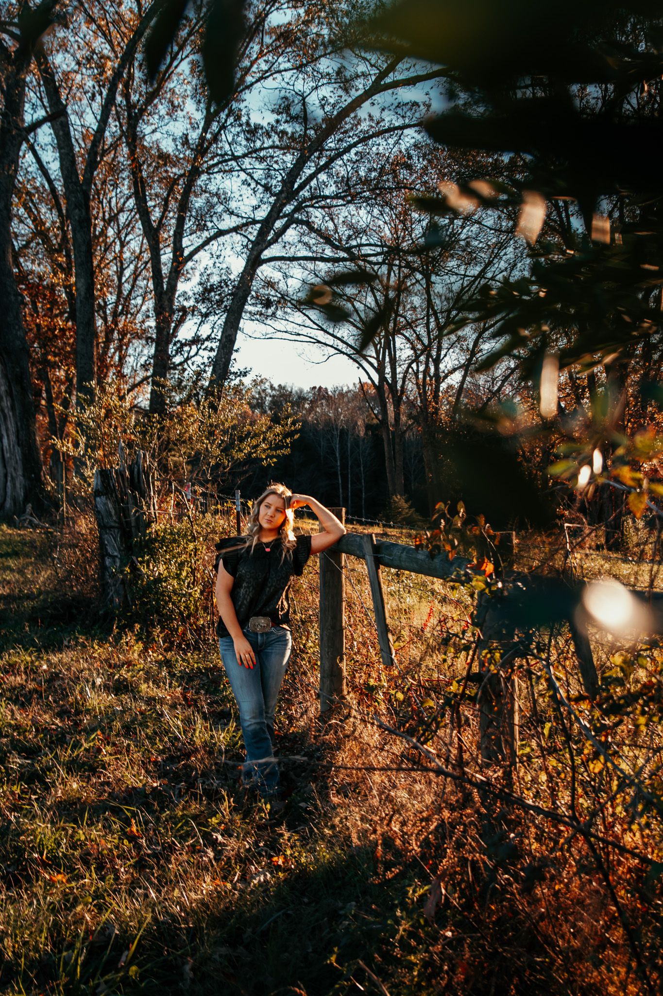 Girl leaning against fence post in the golden sunlight while reflecting on her life that has led her to this moment before graduating.