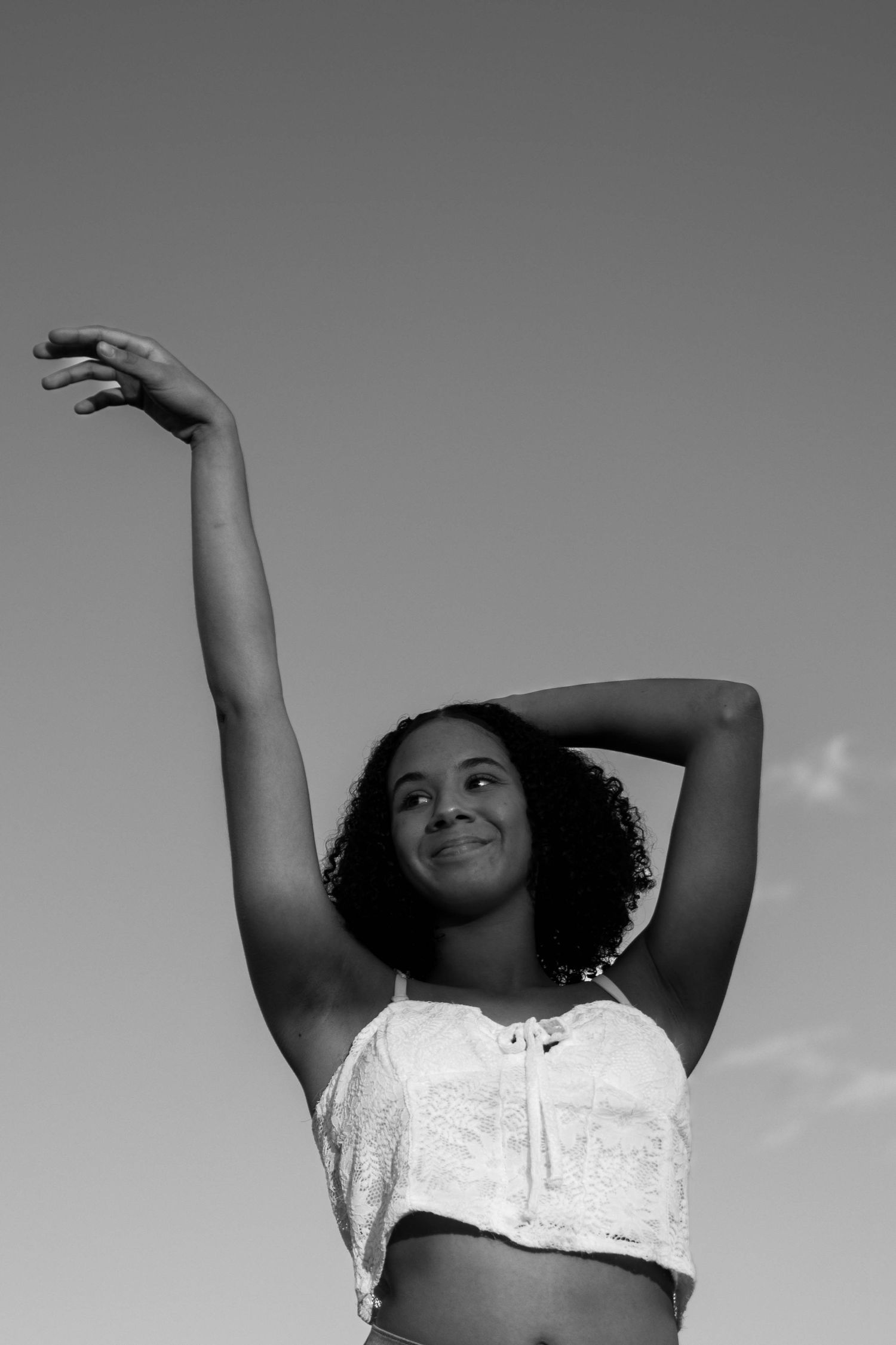 Girl throwing hands up in the air while looking up to the sky celebrating her graduating high school.