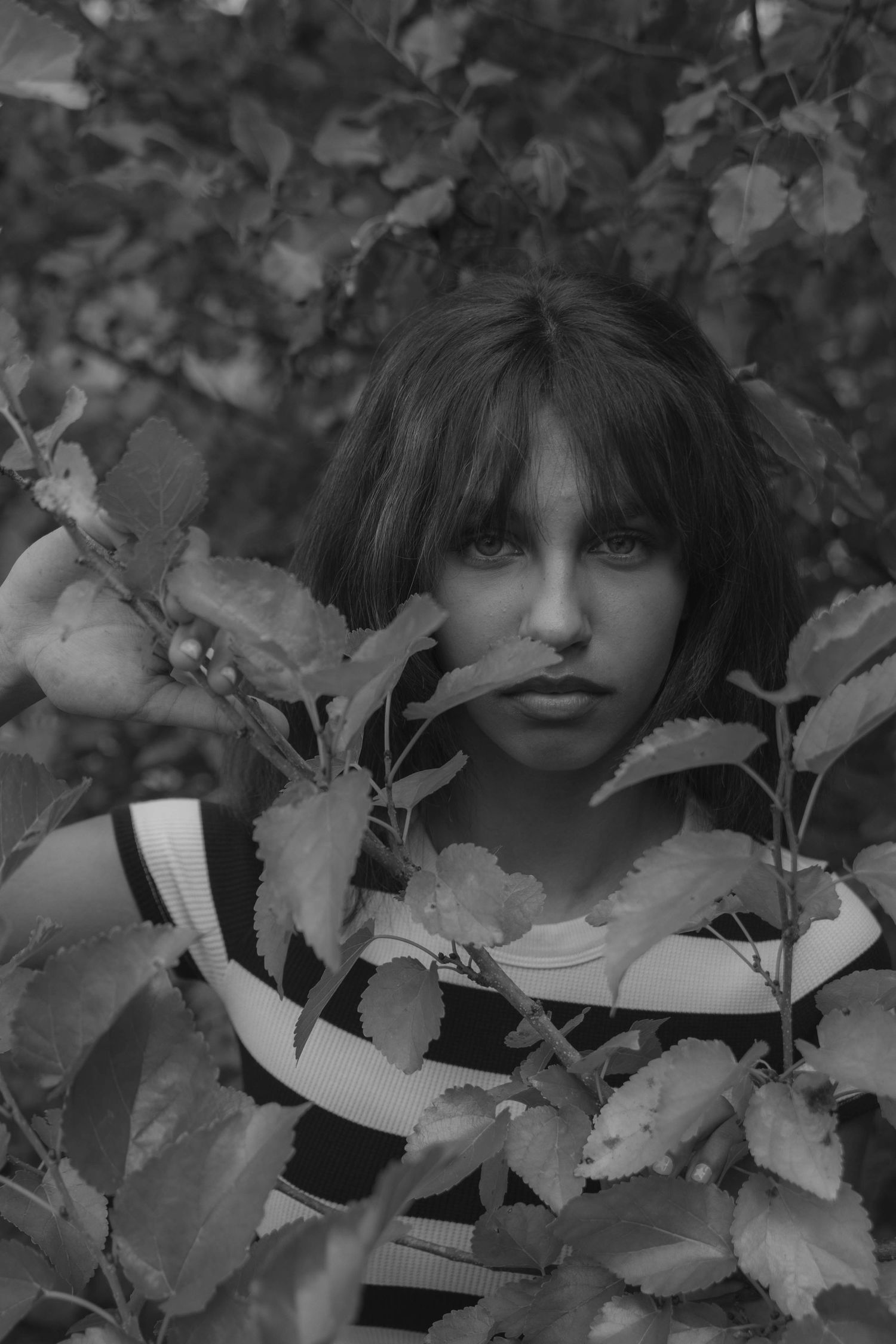 Girl peeking through the green leaves of an overgrown bush of an abandoned drive in.