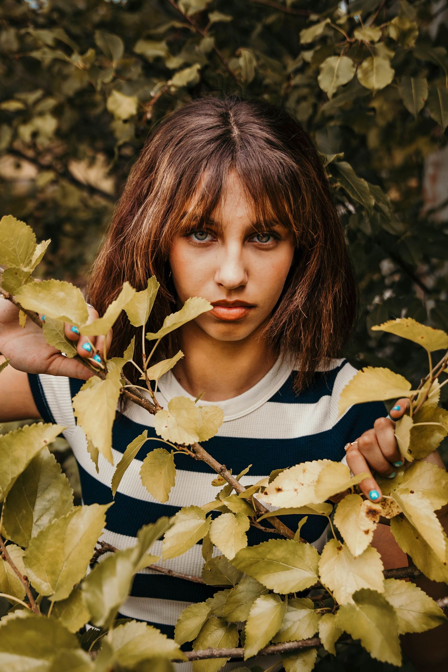 girl peeking out behind green tree branchs