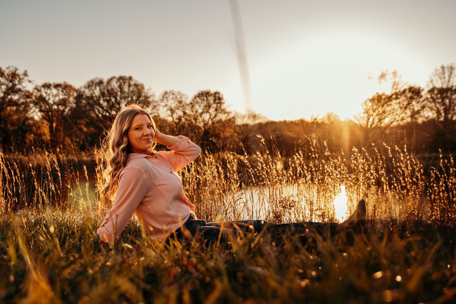 Girl sitting in front of a golden sunset while it reflects on the water and washes her in golden sunlight.