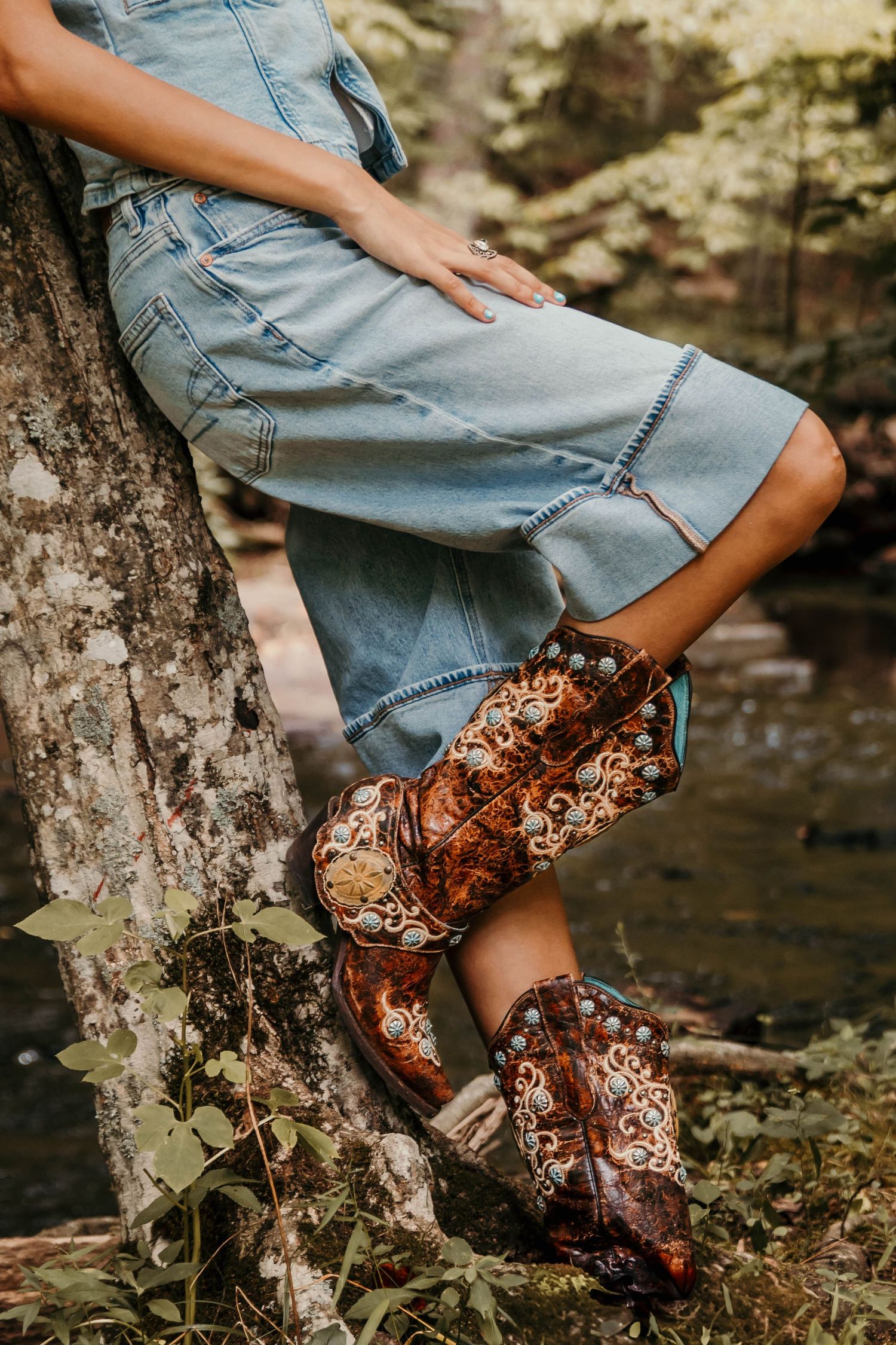 Girl leaned against an old leaning tree that goes over a running creek.