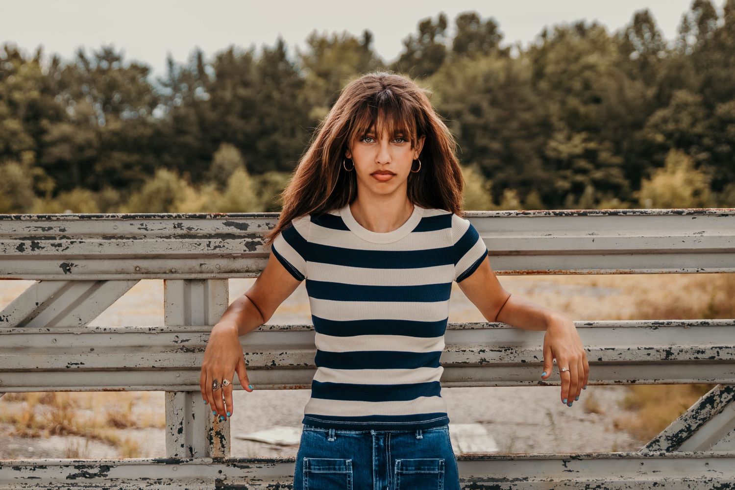 Girl leaning on the opening gate of an abandoned drive in.