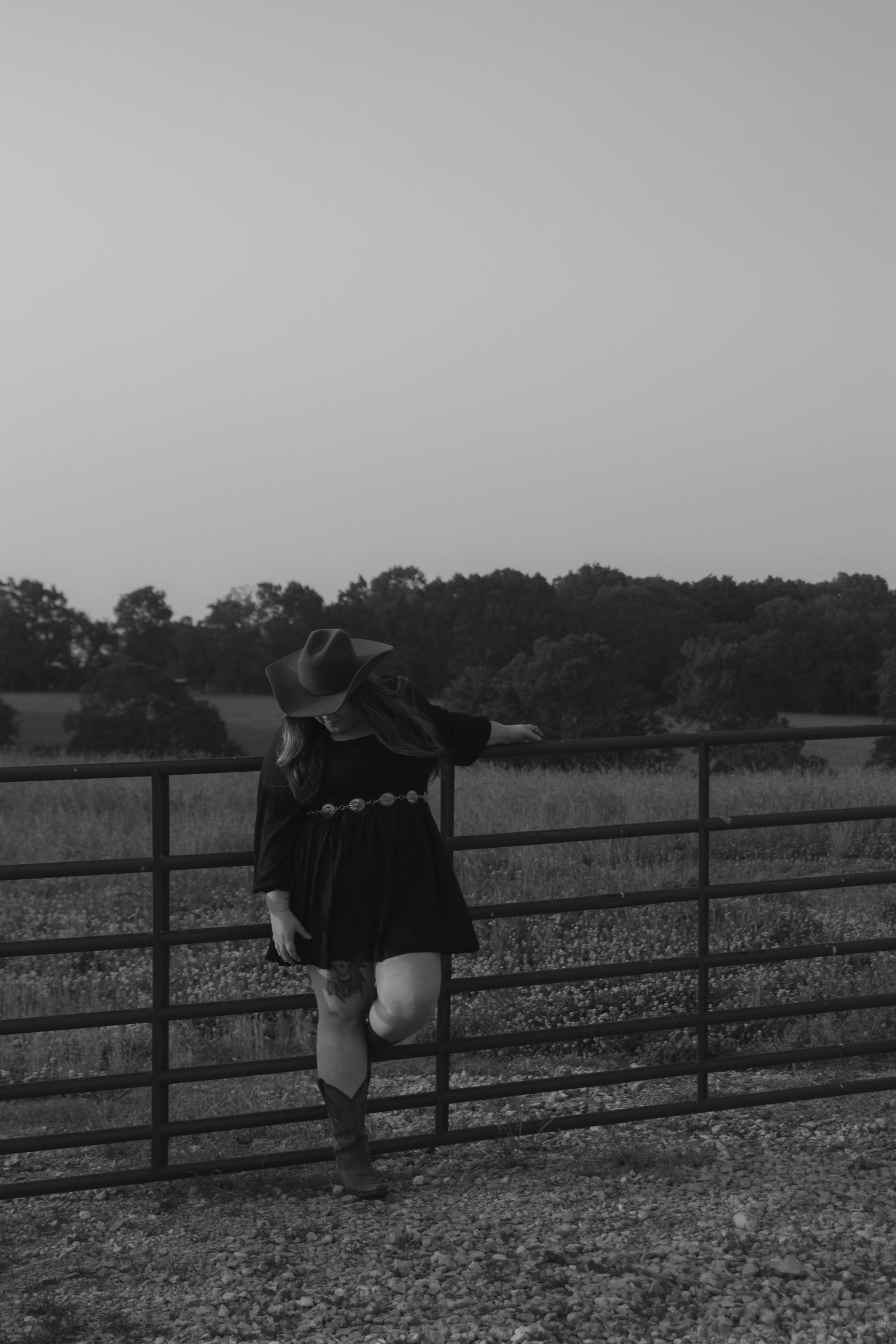Girl in western attire propped against a fence while taking in the moment.