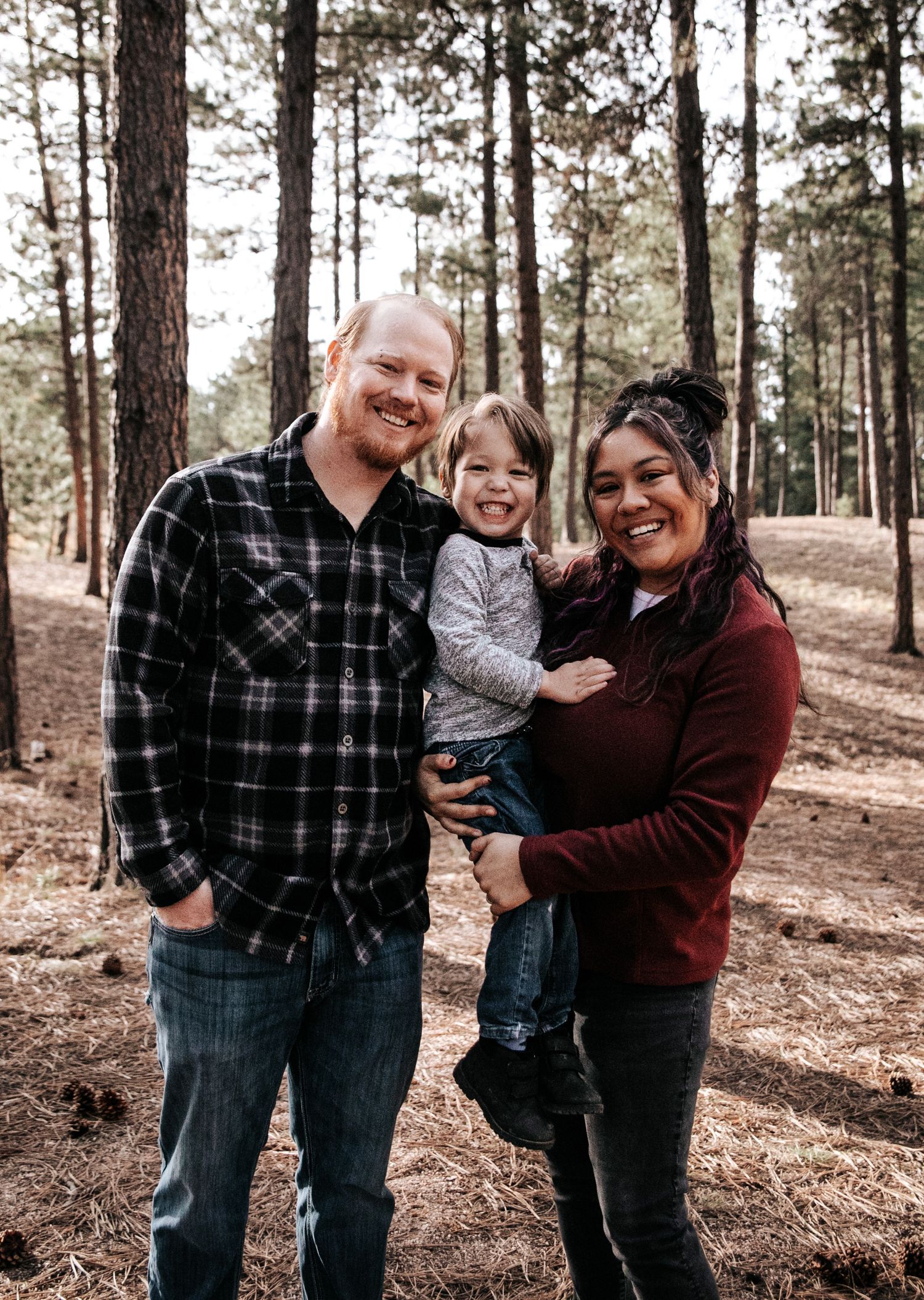 Young family of three posing together in a pine forest.