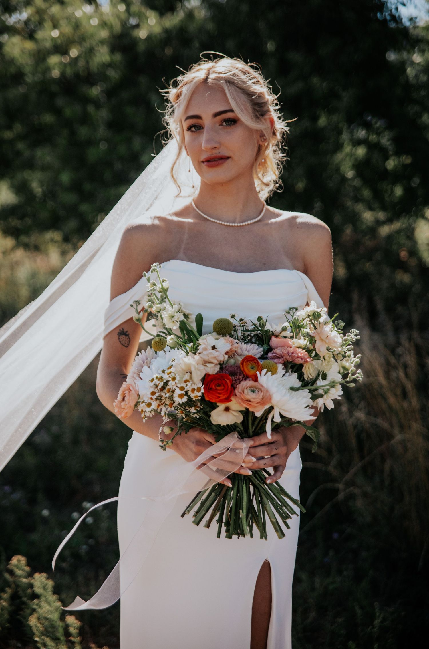 A bridal portrait showcasing a white wedding gown, flowing veil, and vibrant bouquet in natural light.