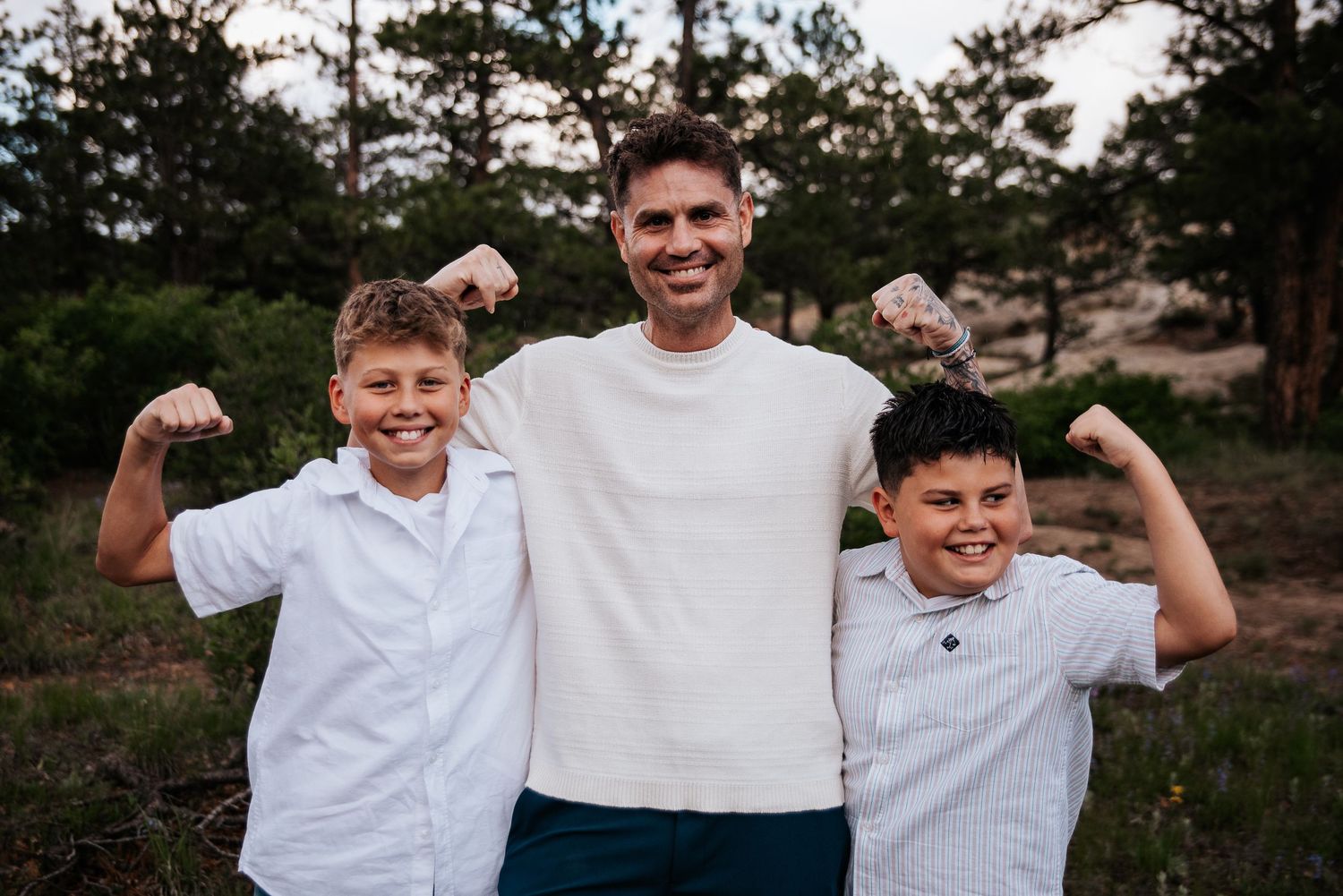 Energetic pose of father and sons with raised arms against mountain backdrop during sunset at Ute Valley Park in Colorado Springs