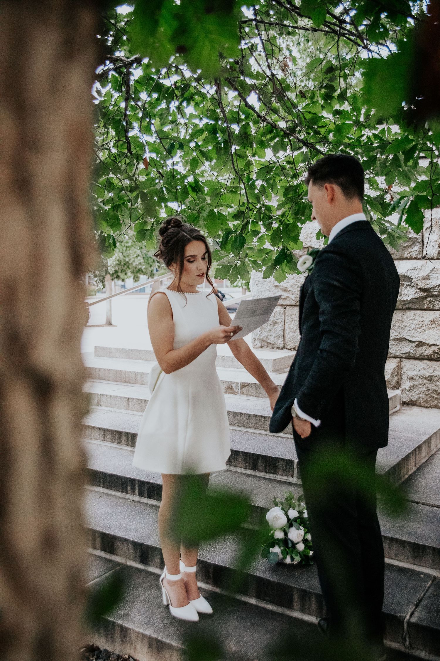 A wedding couple shares an intimate moment on stone steps surrounded by lush green foliage at Colorado Springs courthouse wedding.