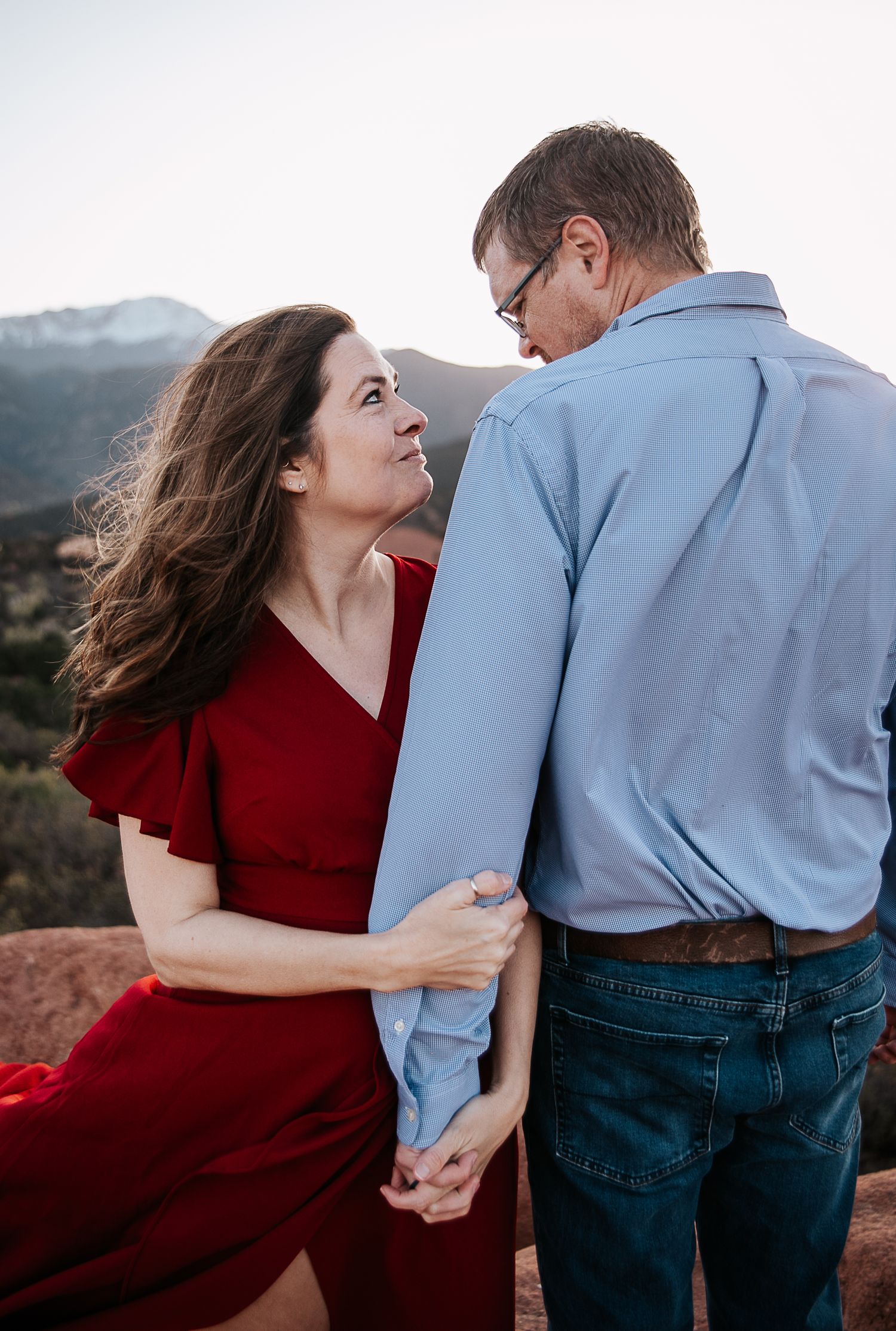 A tender moment between a couple in red and blue attire on rocky mountain terrain.