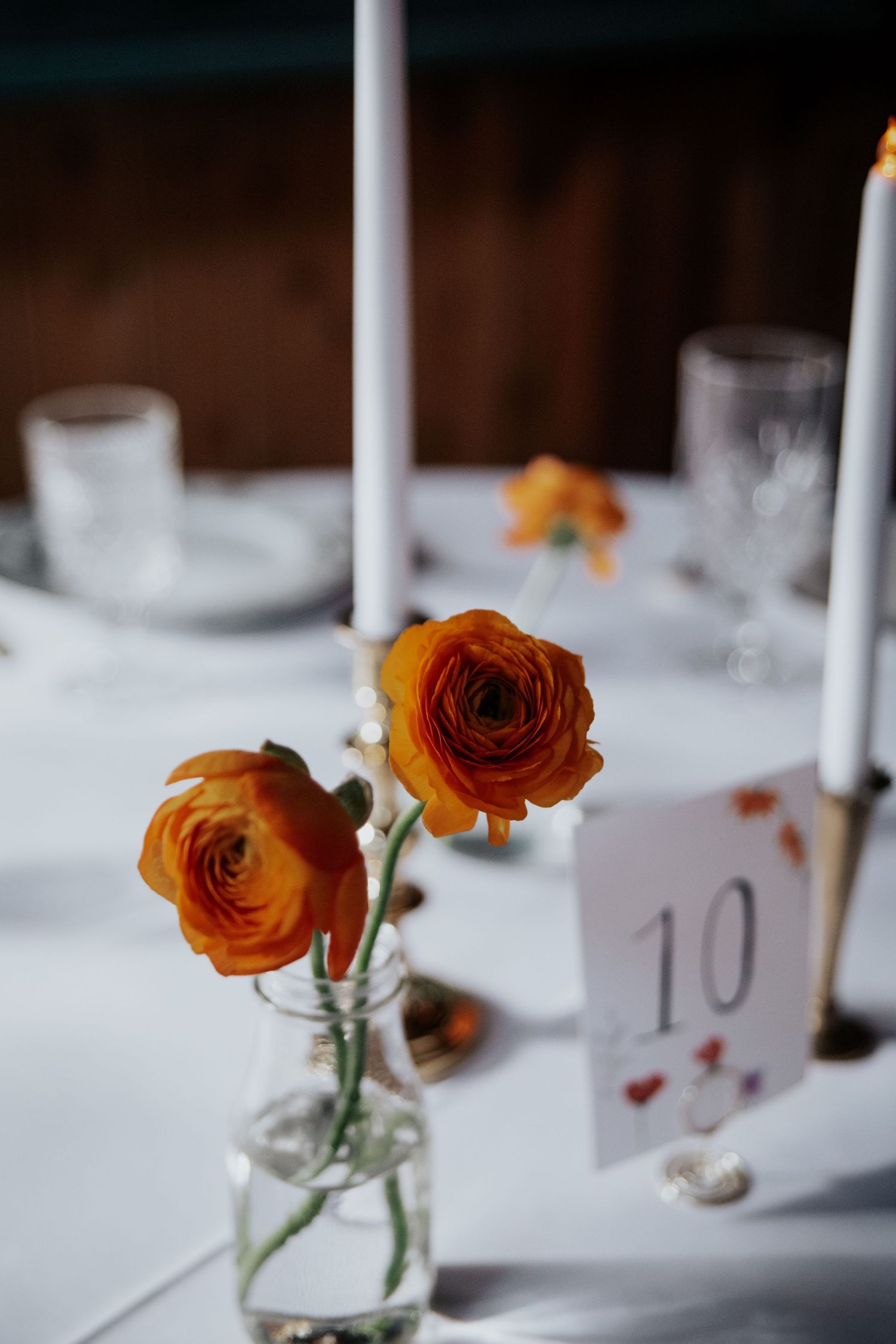 Orange roses in small glass vases with table numbers set on white linens.