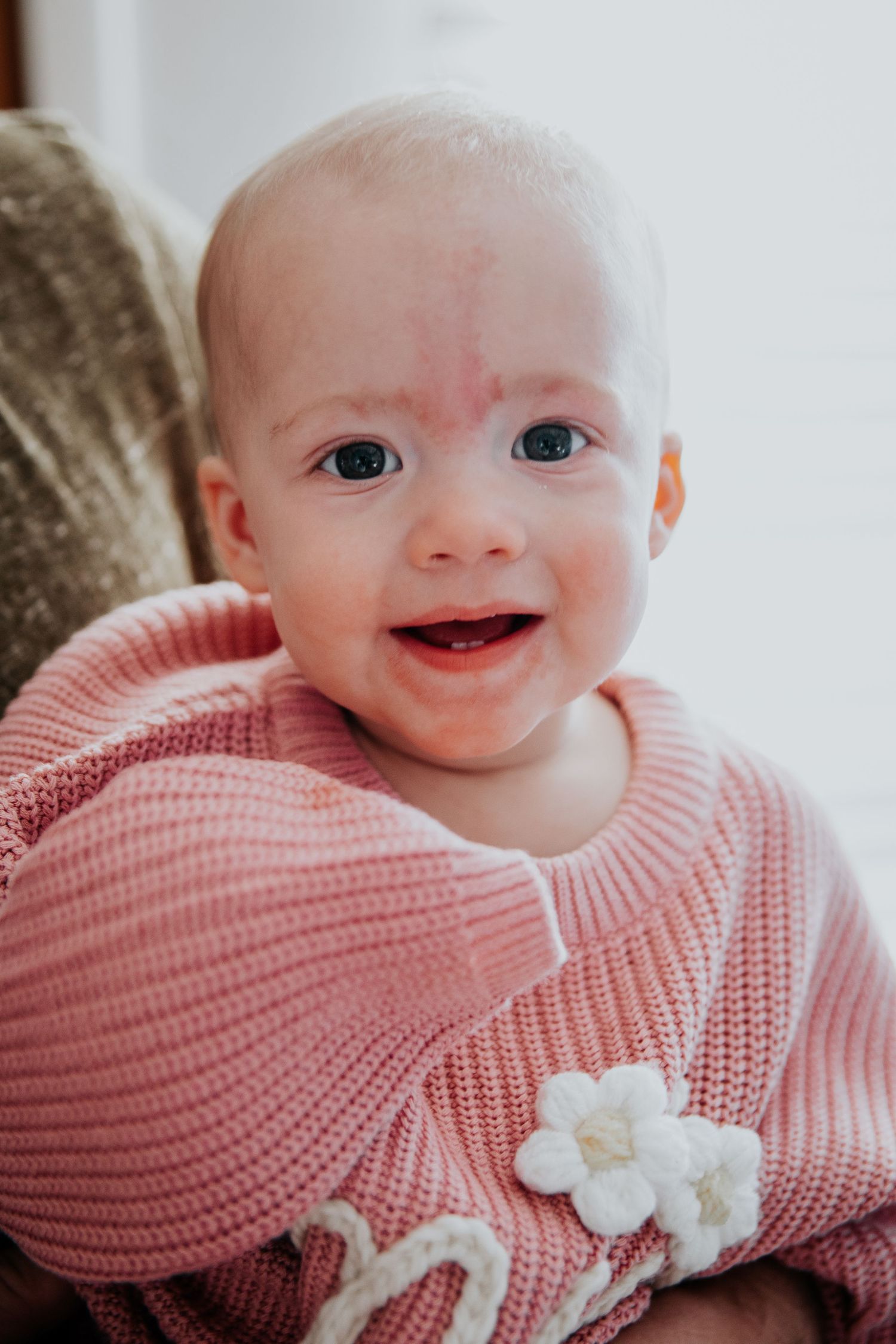 Baby in pink knit sweater shows various expressions while laying down.