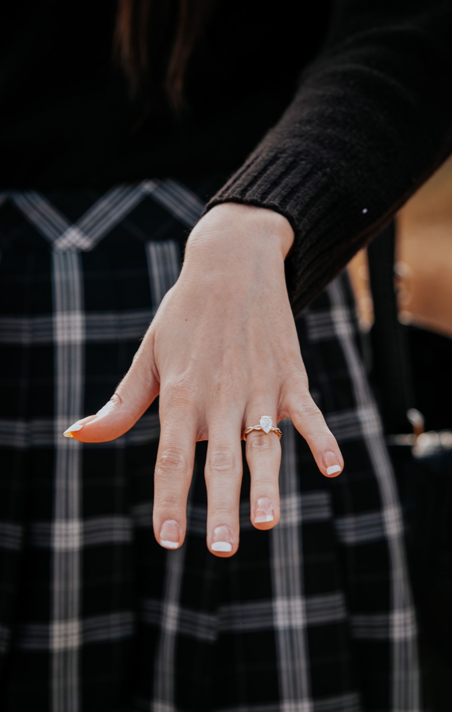Close-up shots of hands displaying an engagement ring against a black and white plaid pattern.