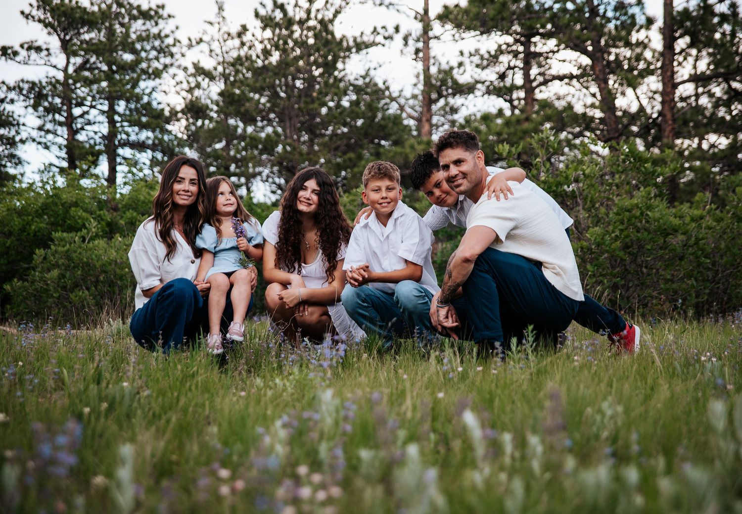 Family lounges together in a grassy meadow with pine trees in the background at Ute Valley Park in Colorado Springs