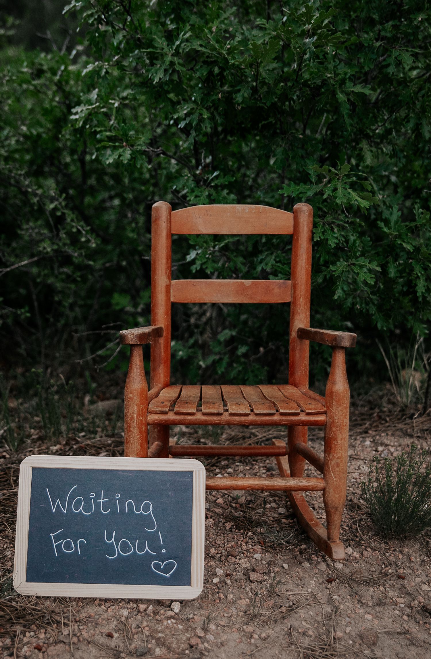 Two wooden rocking chairs with chalkboard signs reading 'Waiting for you' in an outdoor setting.
