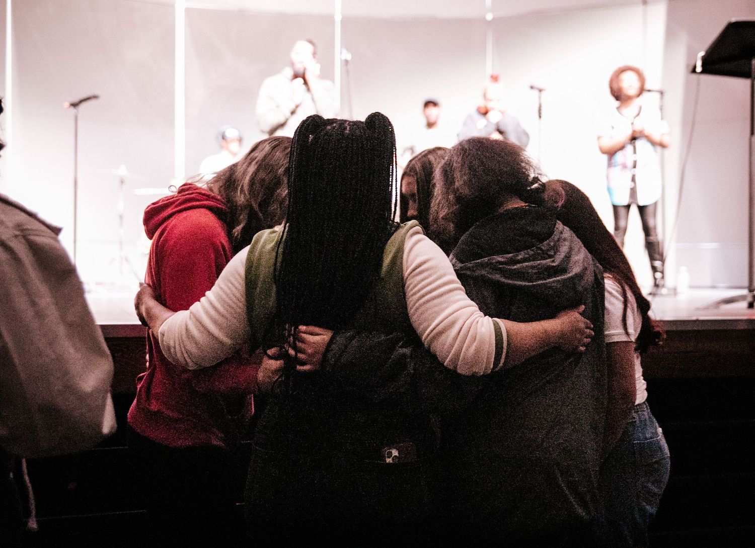 Group huddled together in white lighting during theatrical performance.