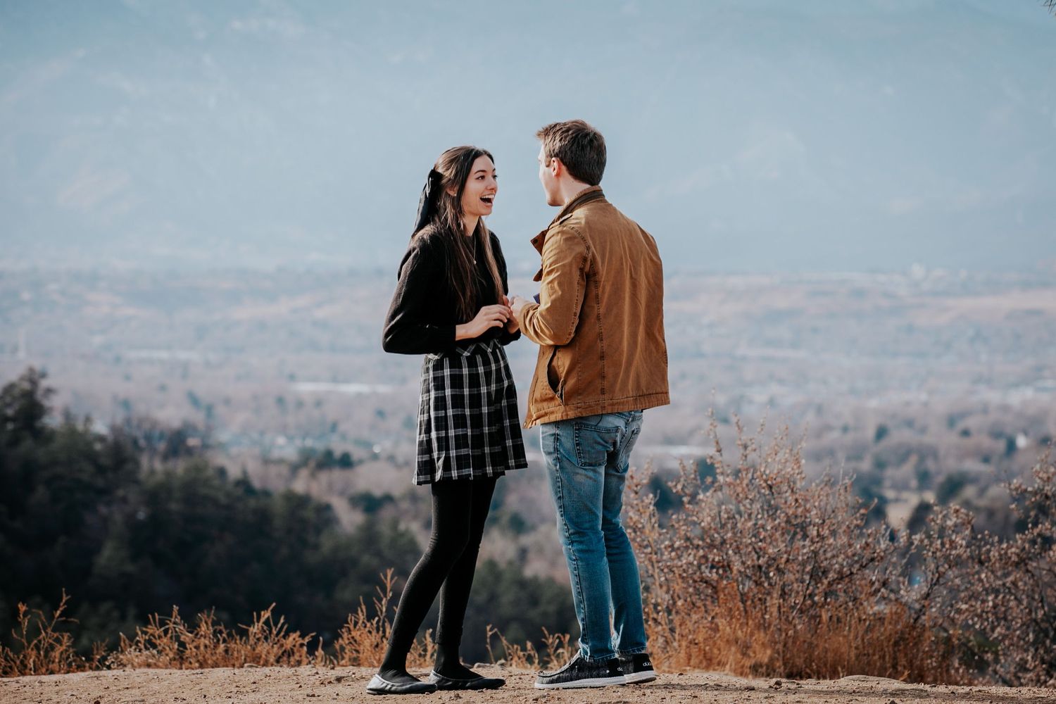 Happy couple celebrates engagement moment on scenic mountain overlook.