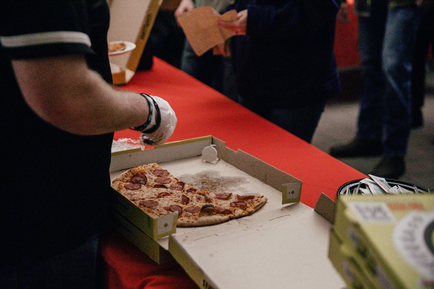 People serve themselves food from a long buffet table with red tablecloths.