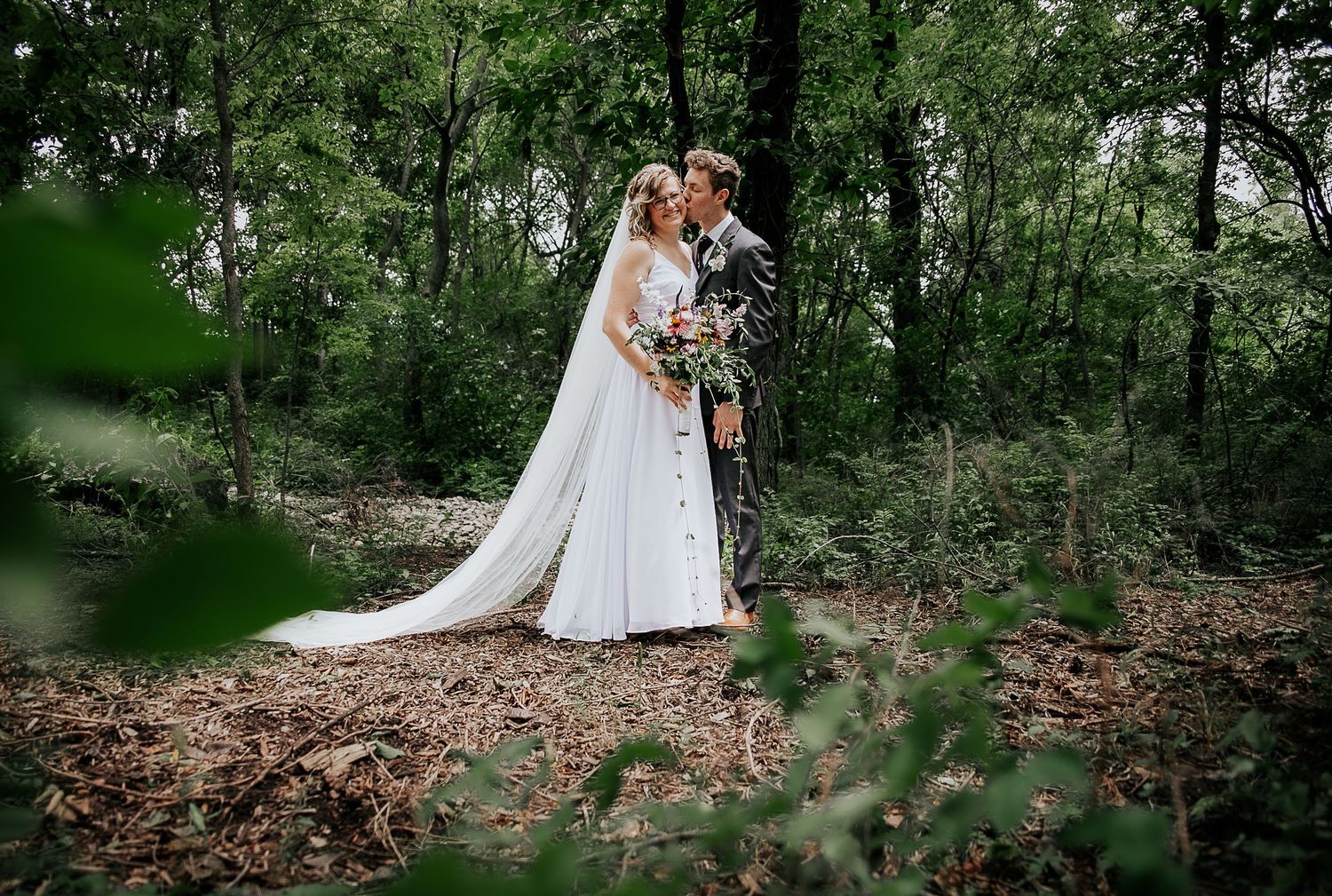 A romantic wedding portrait captured in a serene wooded setting with soft natural lighting.