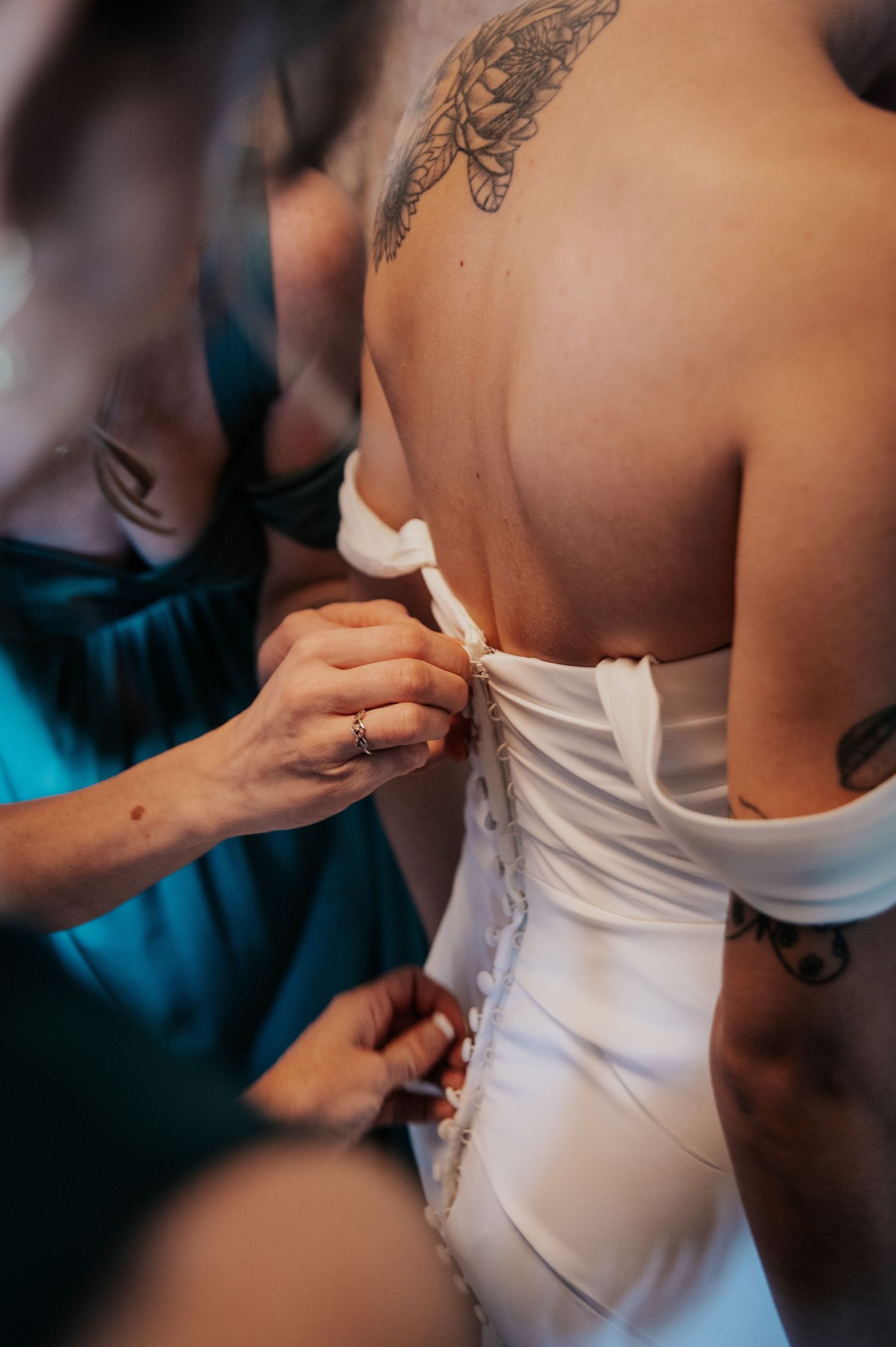 Close up of hands lacing up a white wedding dress corset with visible butterfly tattoo.