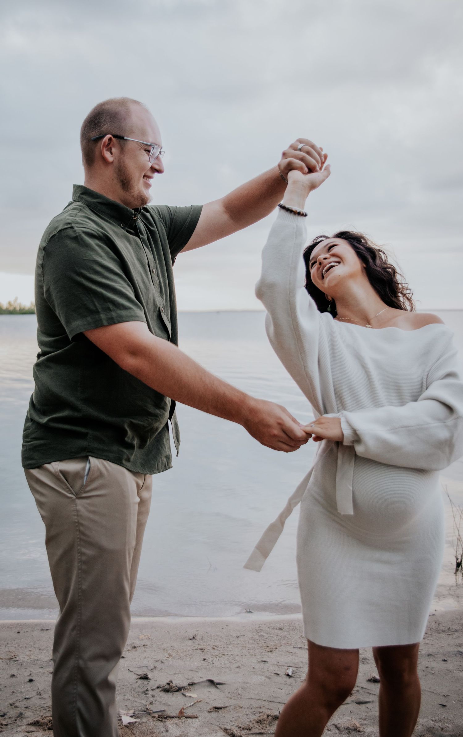 A playful couple shares a fun moment together on a beach during an overcast day.
