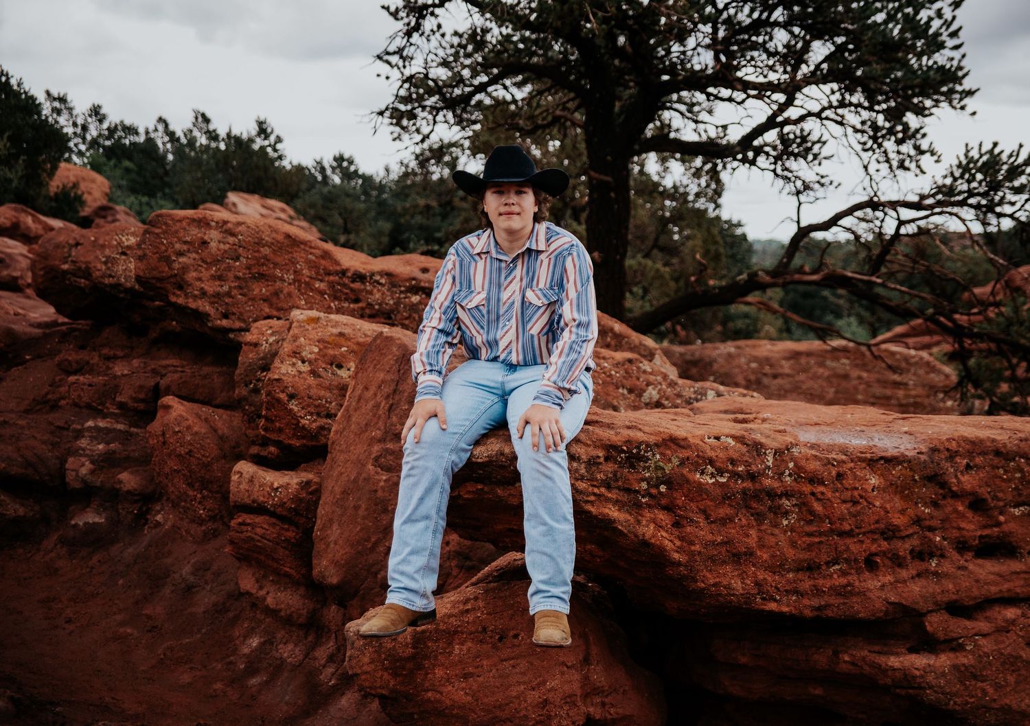 A high school senior in western attire poses against a scenic mountain backdrop at Garden of the Gods in Colorado Springs