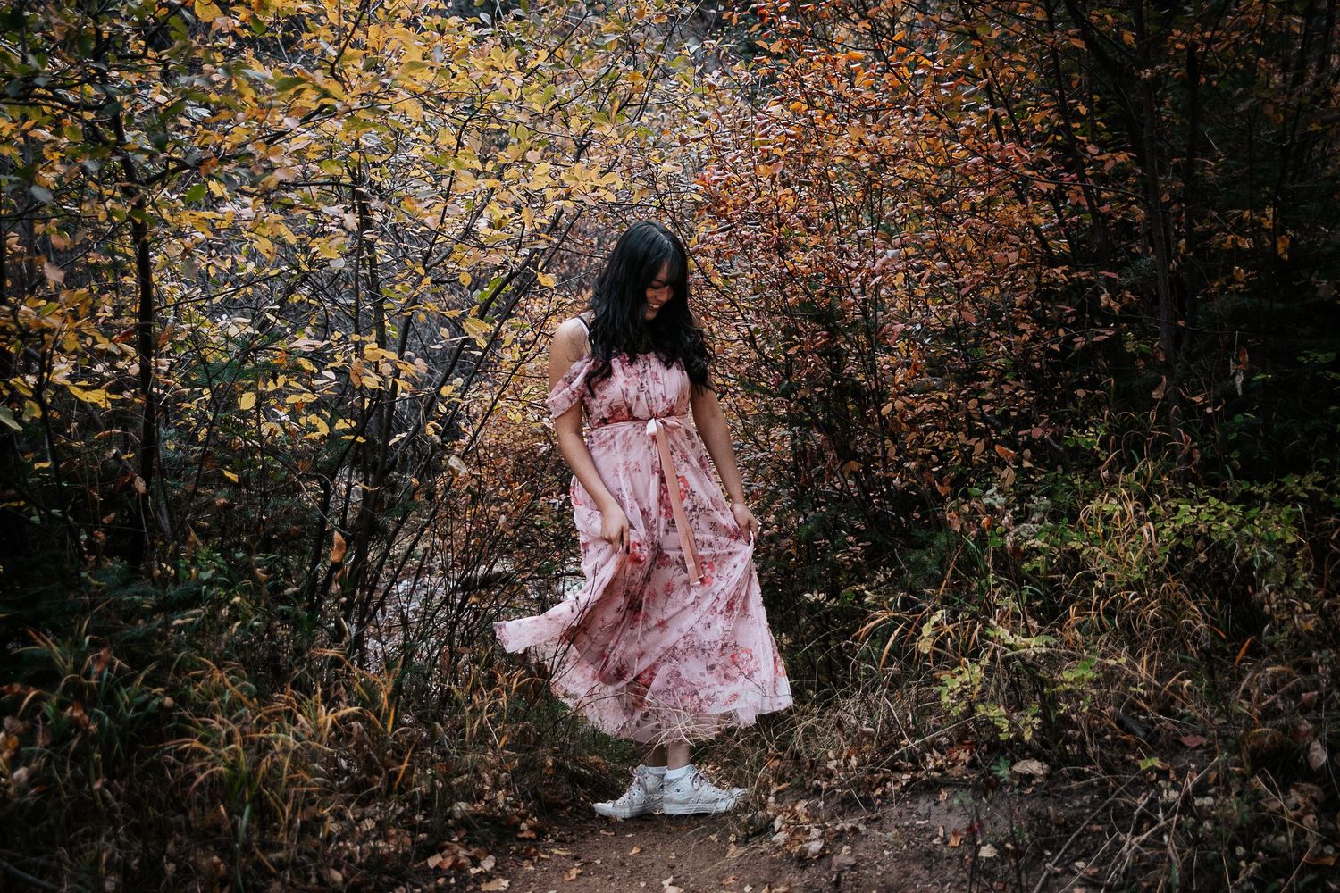 A flowy pink dress twirls against autumn foliage in a forest setting.