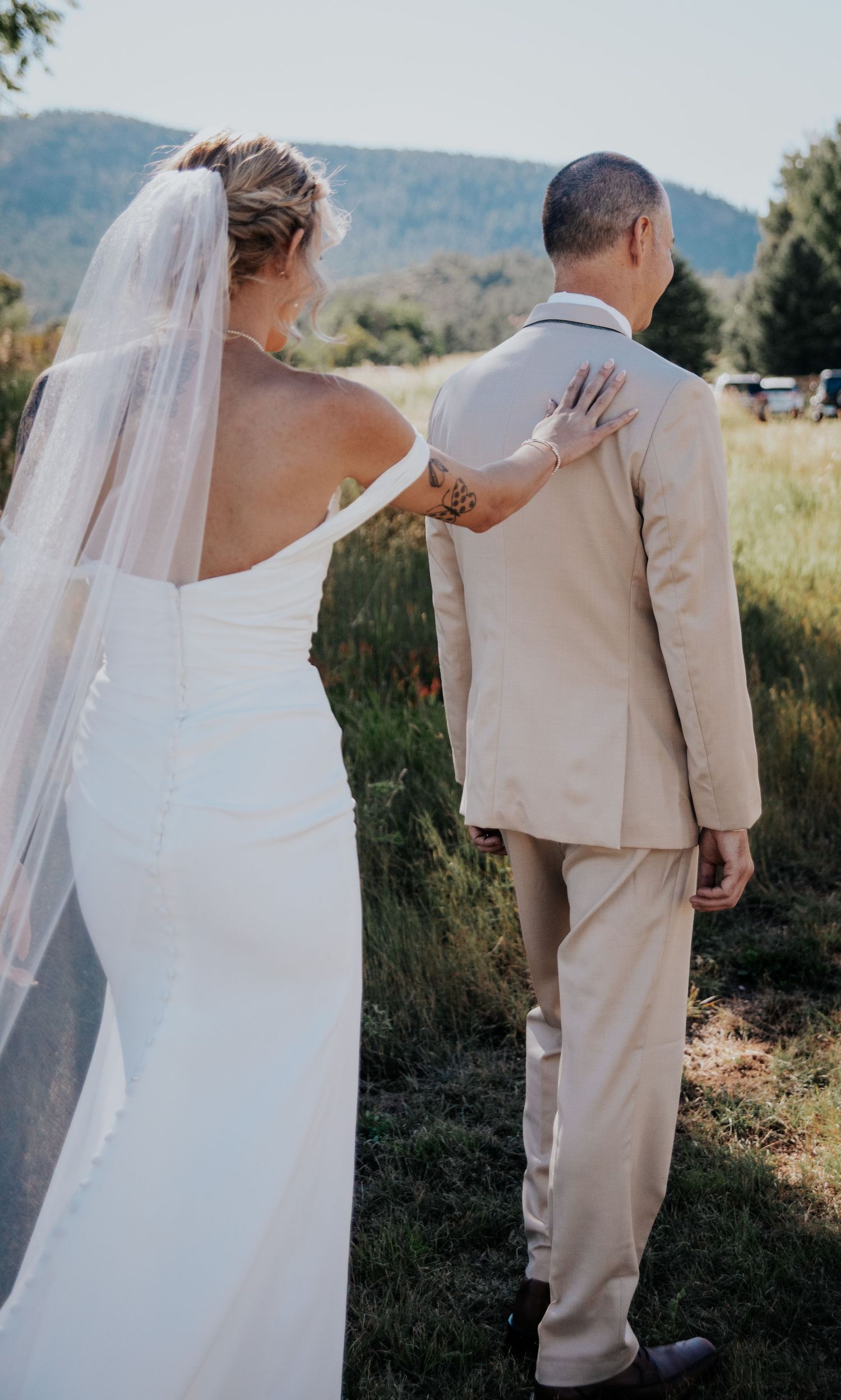 A tender wedding moment captured outdoors with mountains in the background.