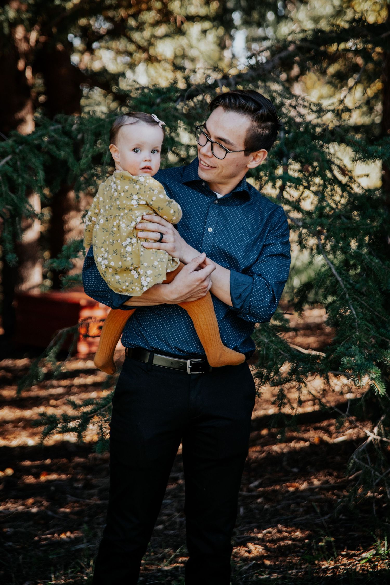 A tender family moment captured in dappled sunlight beneath trees.