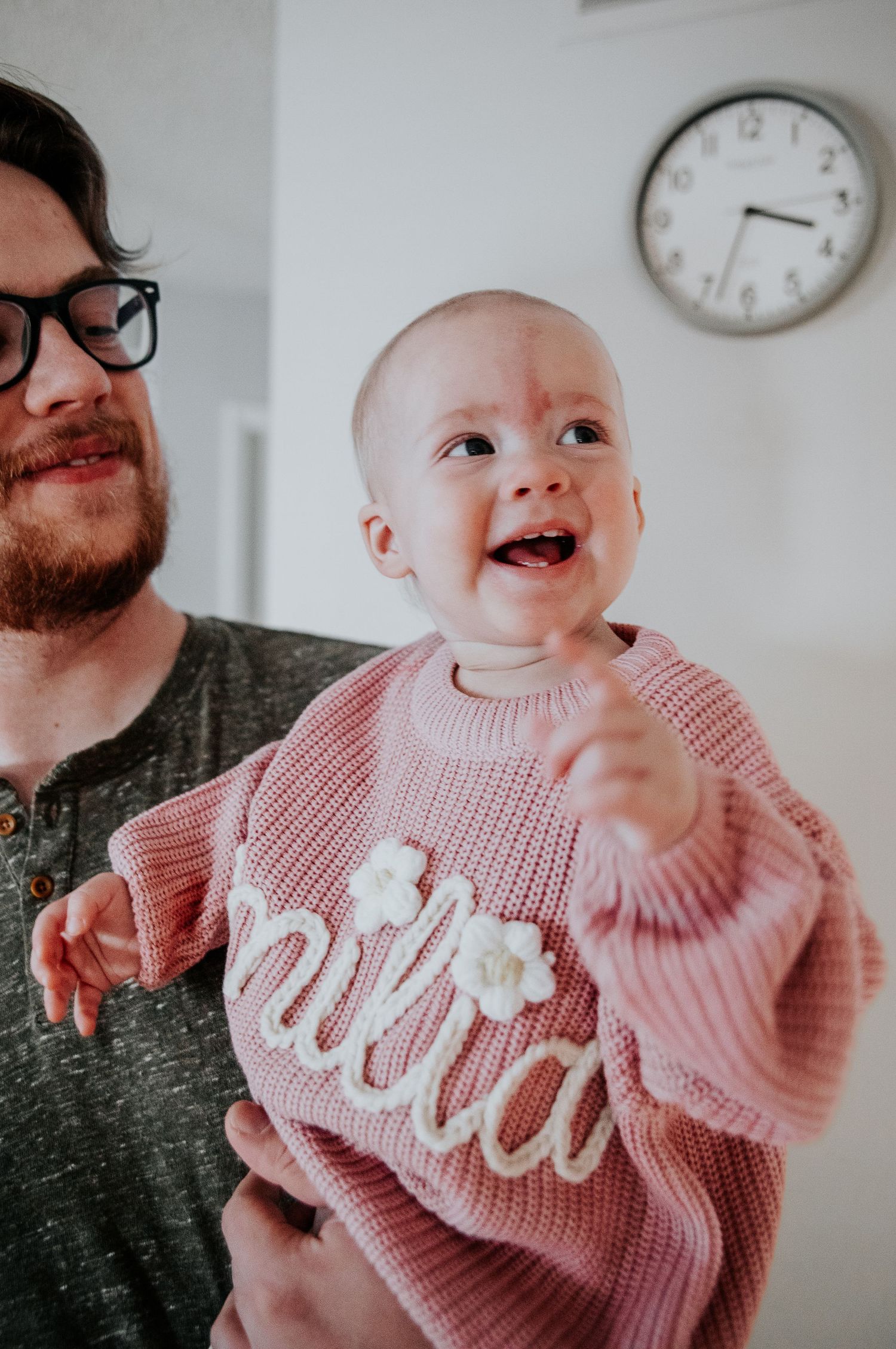 Happy baby in pink sweater shares playful moment with parent.