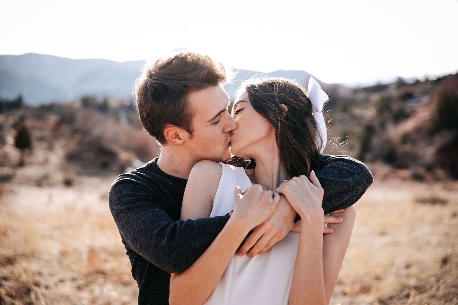 Romantic kiss shared between couple outdoors with mountains visible in background.