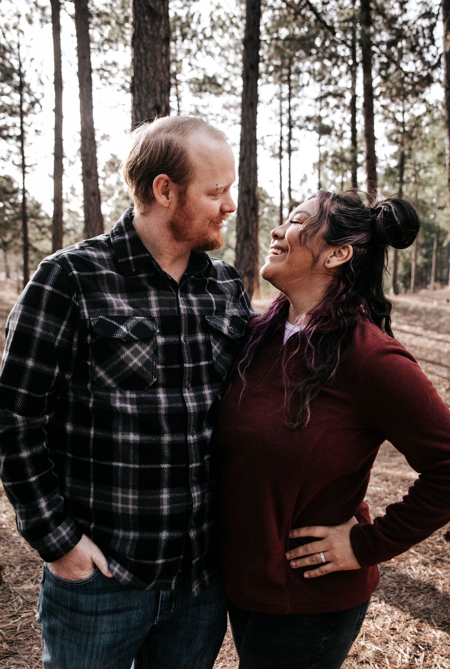 Romantic couple in casual attire sharing playful moments in forest setting.