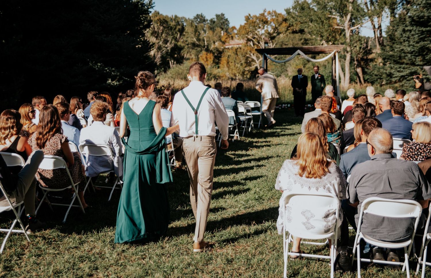 Wide angle view of outdoor wedding ceremony seating with guests in attendance.