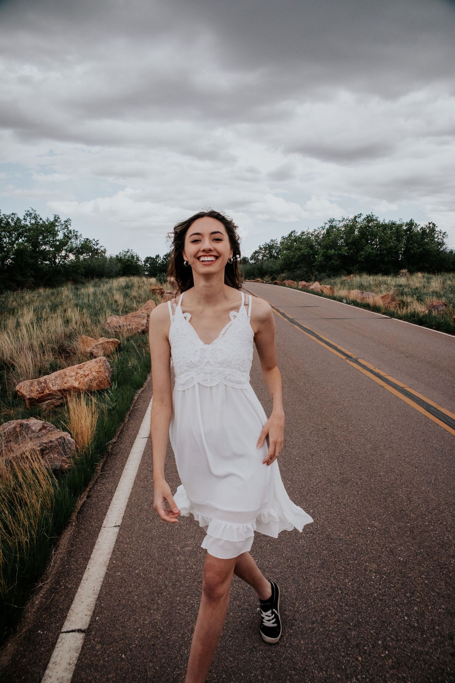 A person in white spins and dances playfully on an empty rural road.