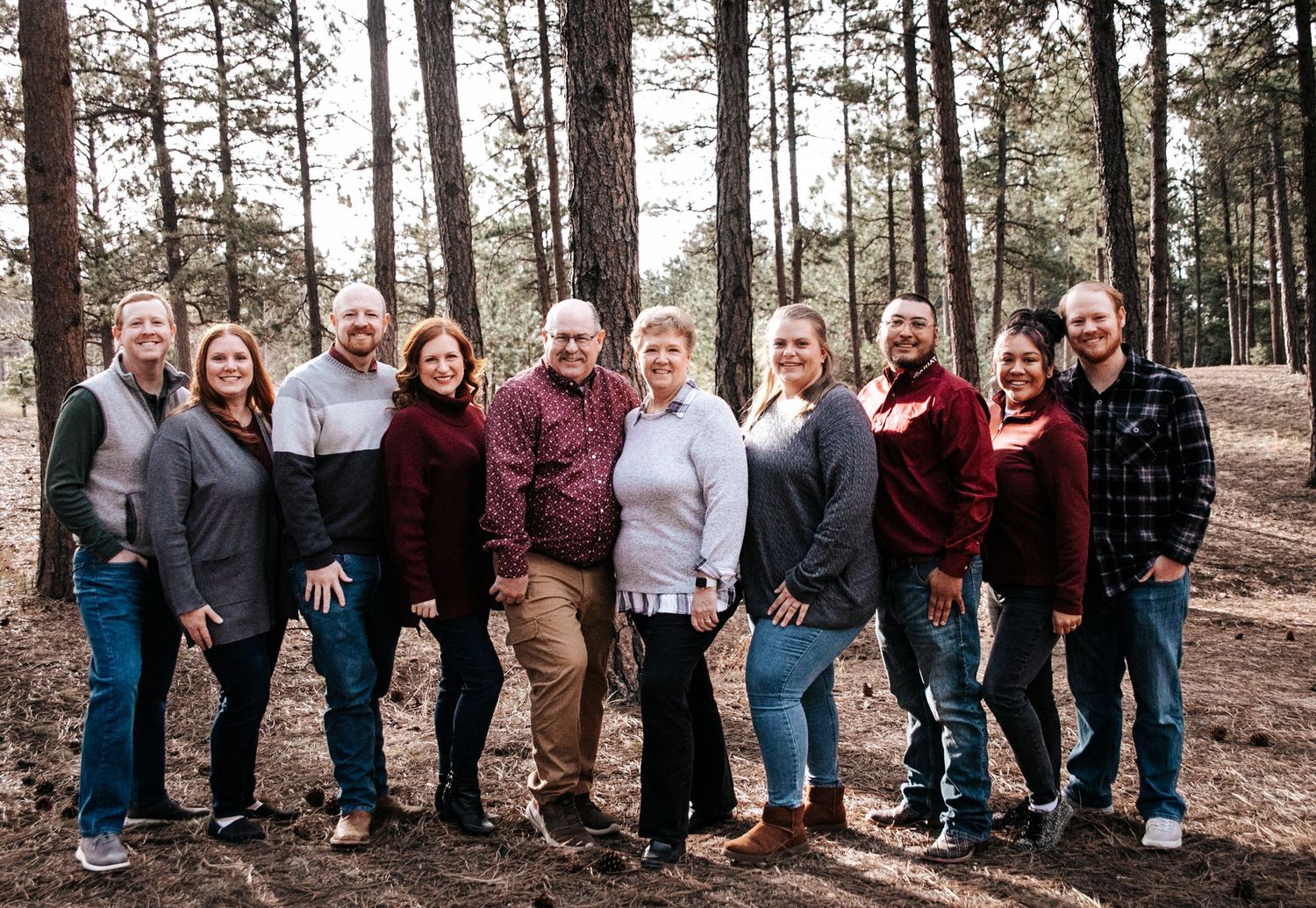 Extended family group photo showing multiple generations lined up against pine trees.