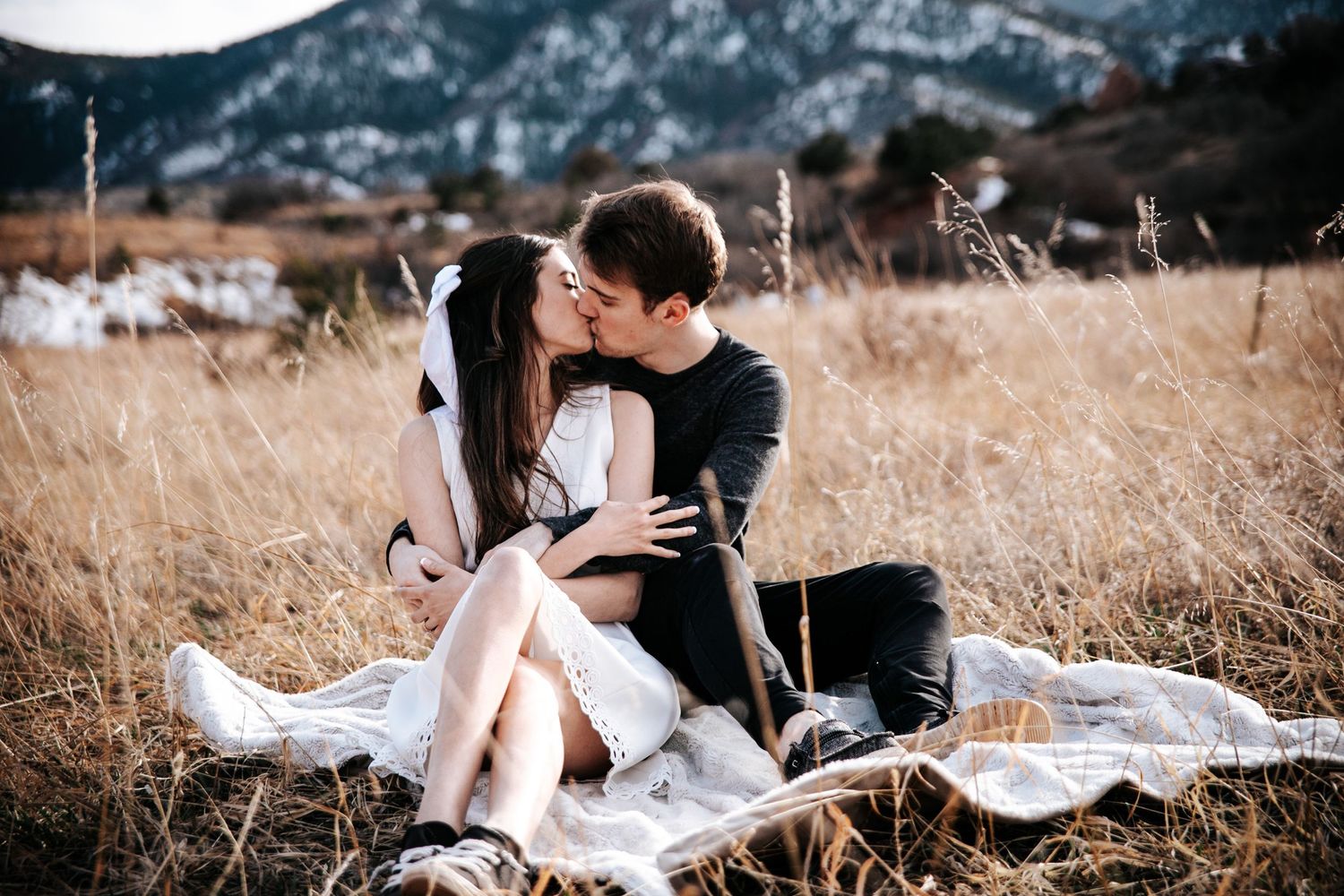Couple sharing an intimate moment on a blanket in a field with mountains in the distance.