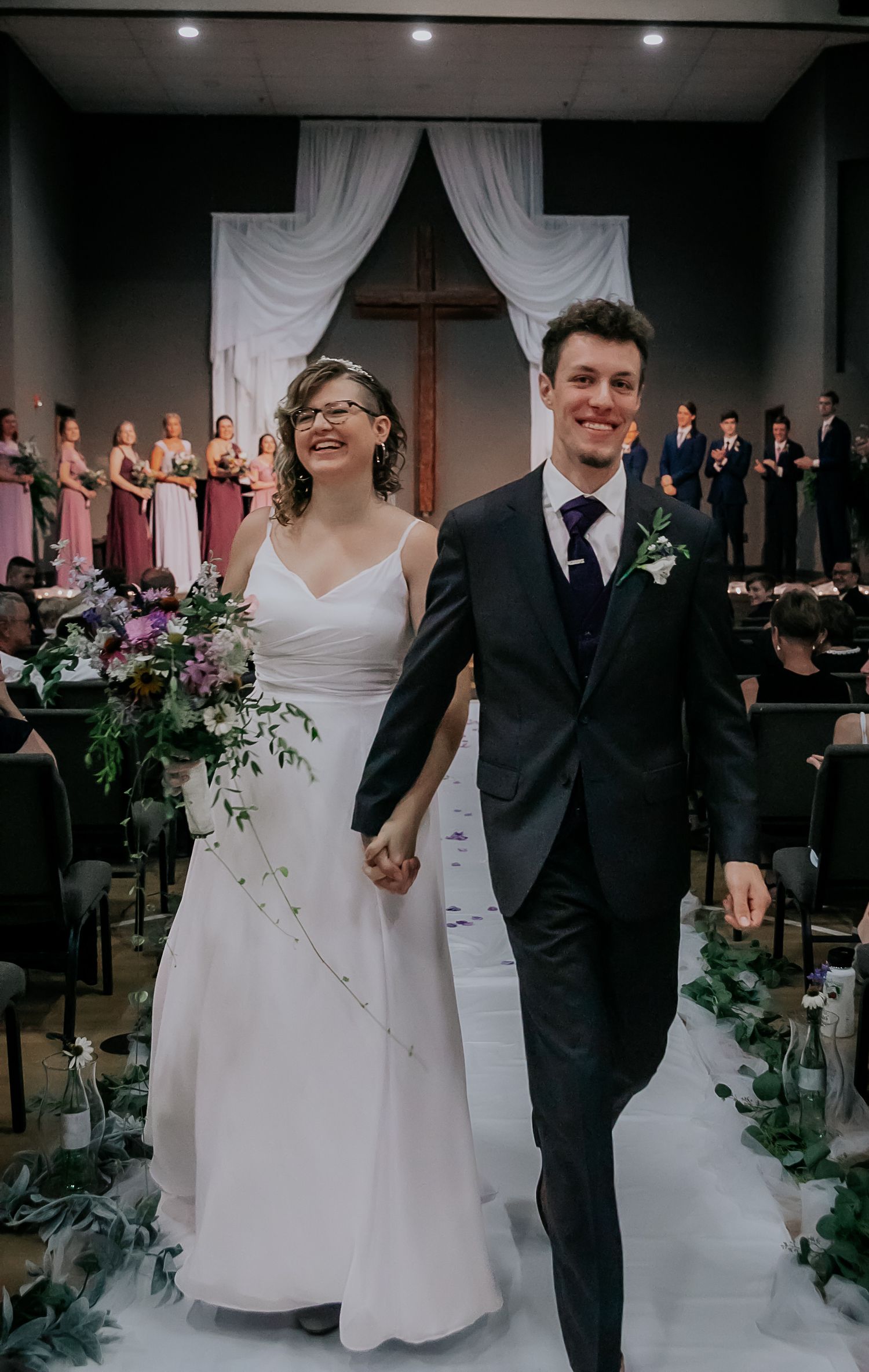 Wedding ceremony in indoor venue with white draping and floral decorations.