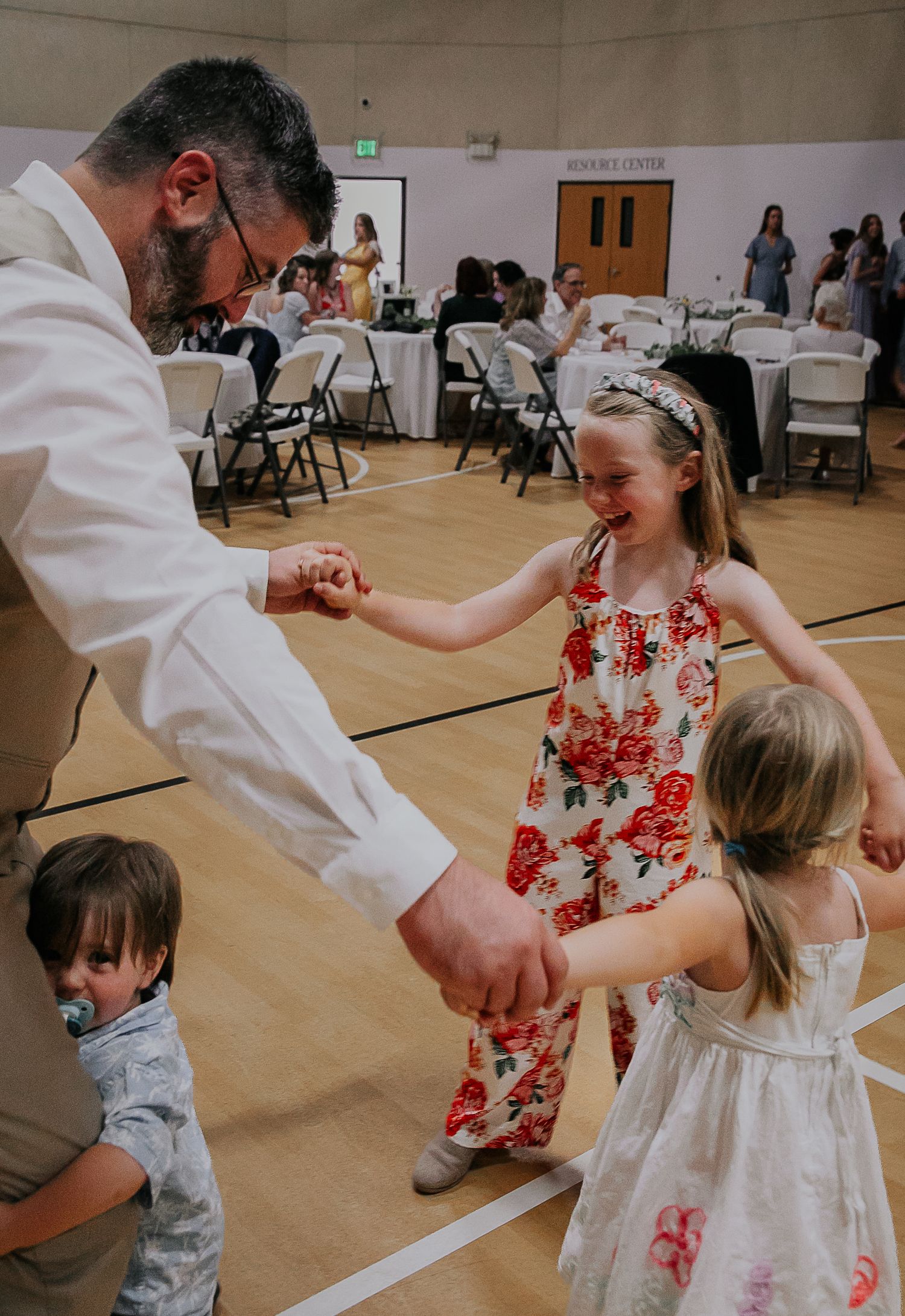 People dancing and celebrating at a lively indoor reception in a community hall.