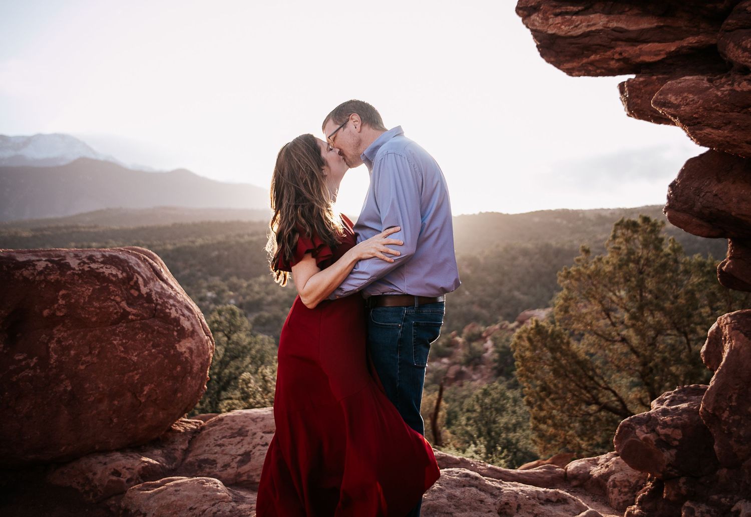 Couple sharing an intimate moment on rocky mountain overlook during golden hour.