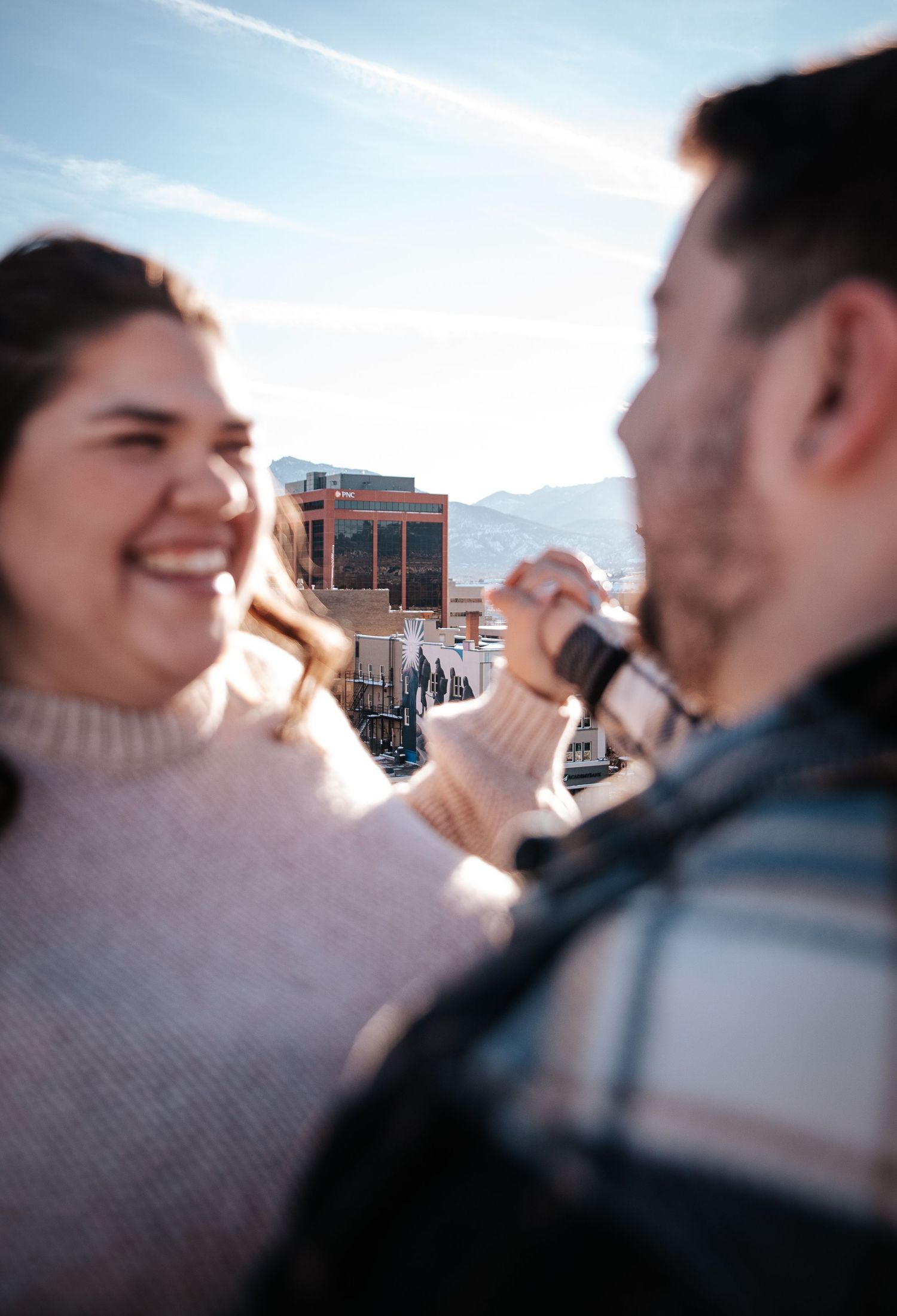 Couple dancing with downtown Colorado Springs behind in focus during golden hour outdoor winter engagement photo session