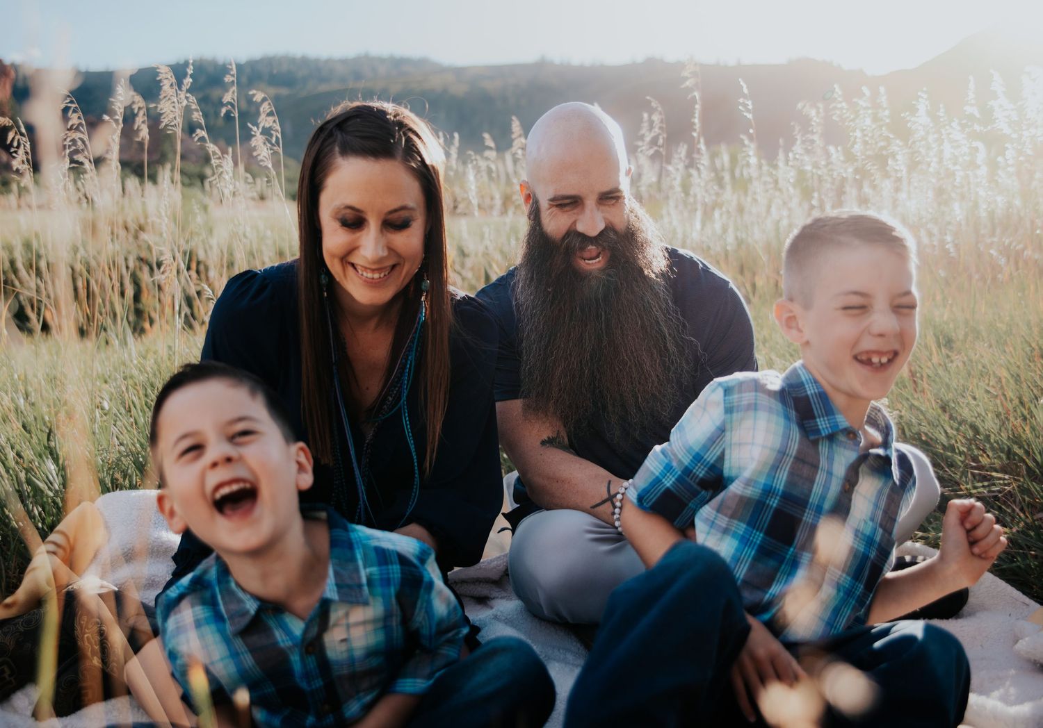 Family laughs together during candid outdoor portrait session in tall grass at sunset.