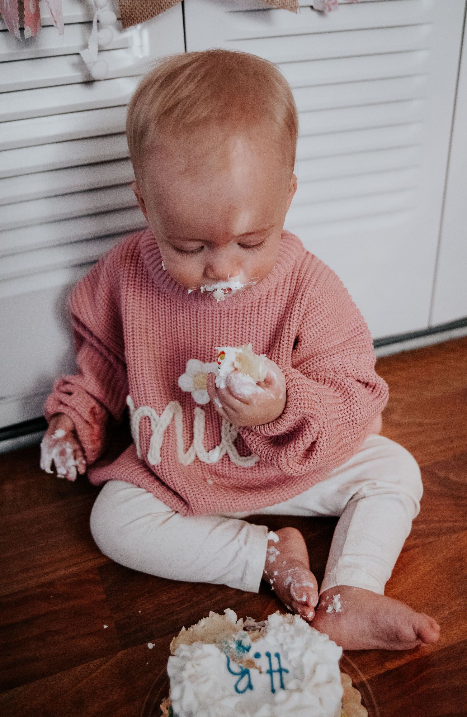 Baby covered in white frosting during messy first birthday cake smash photoshoot.
