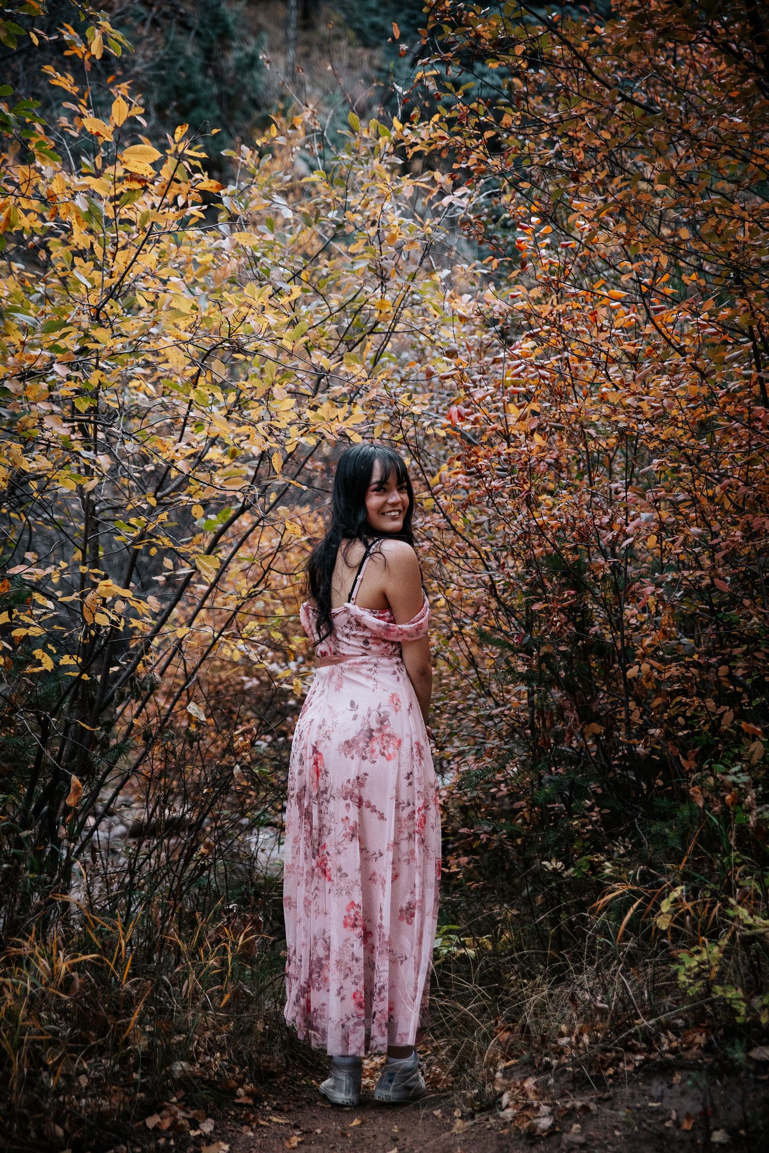 A soft pink dress stands out against vibrant fall foliage in a natural setting.