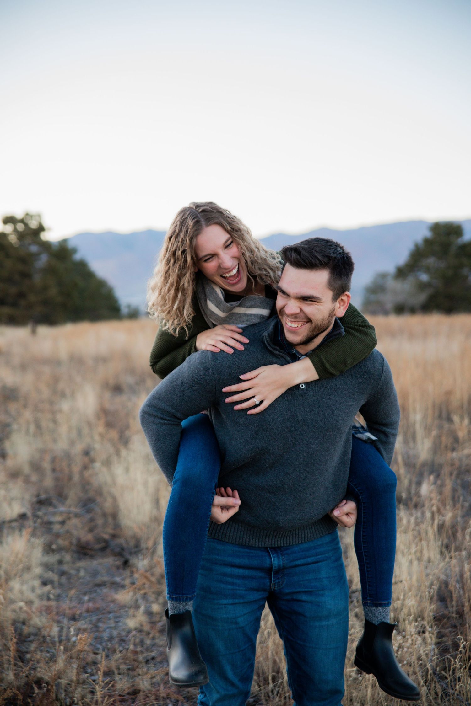 Couple riding piggyback in Palmer Park with mountains in the background during Colorado Springs engagement photo session