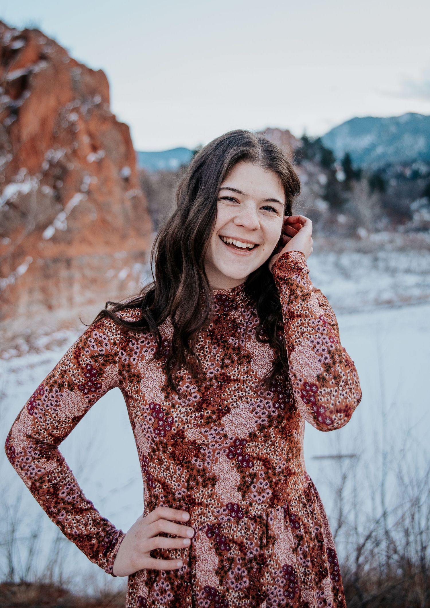 Winter portrait session featuring a floral patterned dress against mountain scenery.