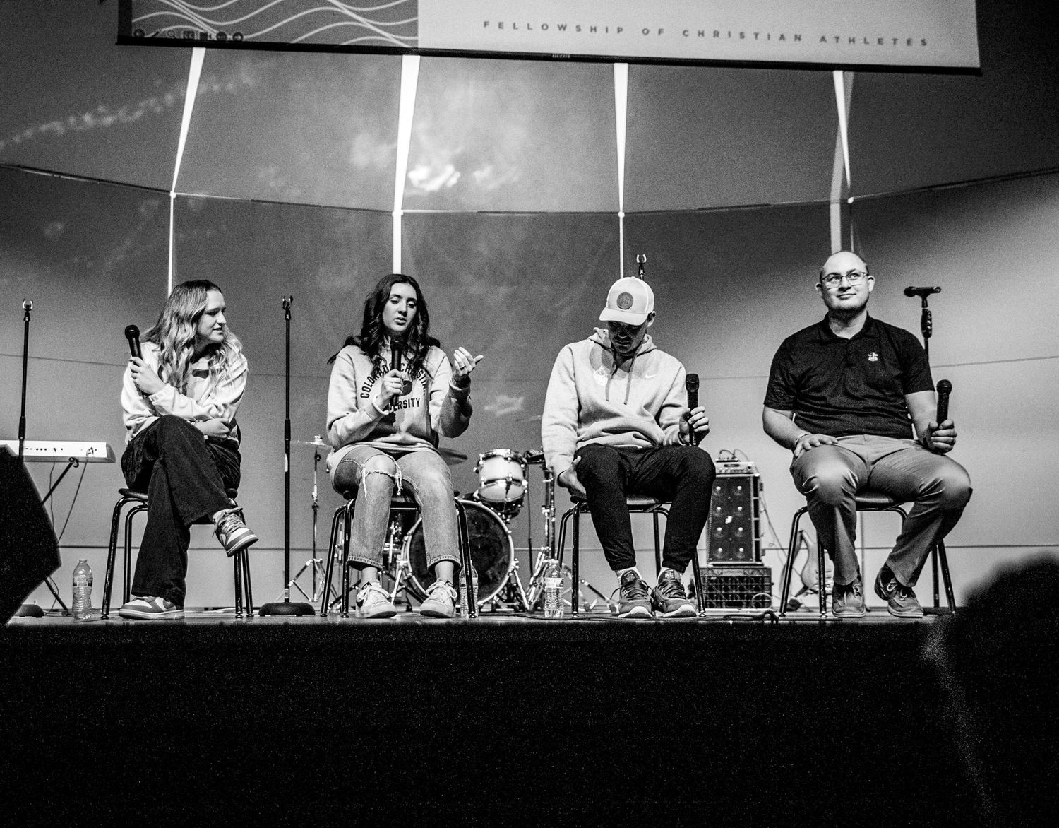 Panel discussion with speakers sitting on chairs on stage in black and white.