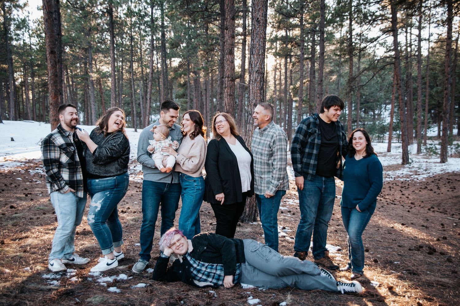 Extended family members pose casually together in a winter forest landscape.