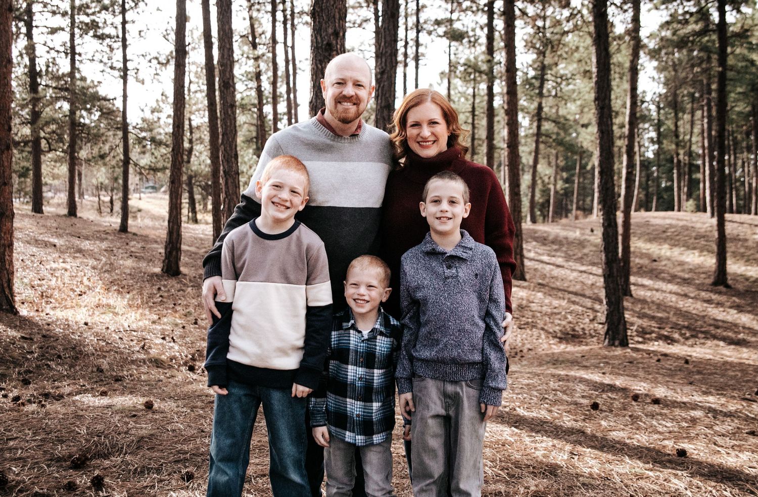 Family of five posing together in a wooded forest setting.