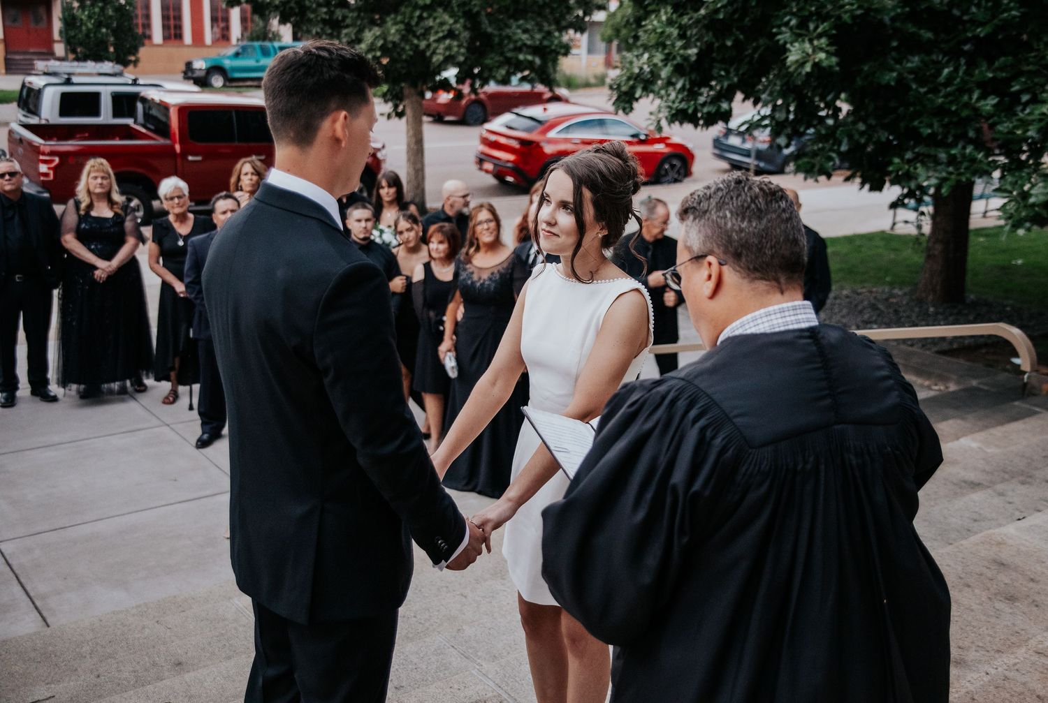 Wedding guests and party members socializing on tree-lined street.
