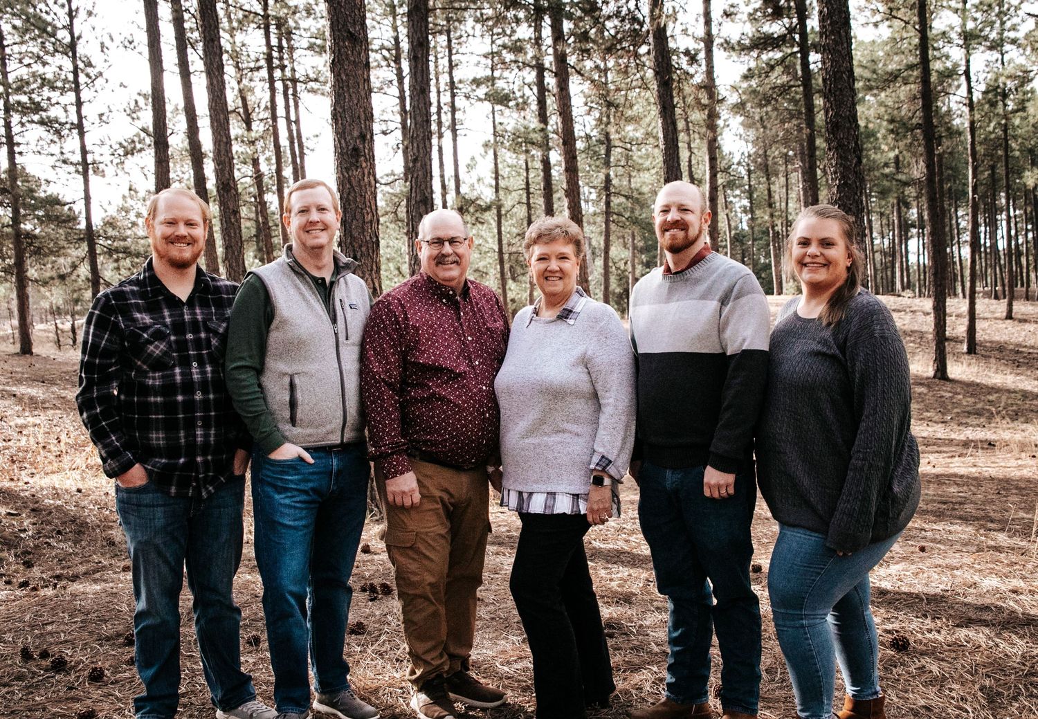 Group portrait of adults standing together in a pine forest.