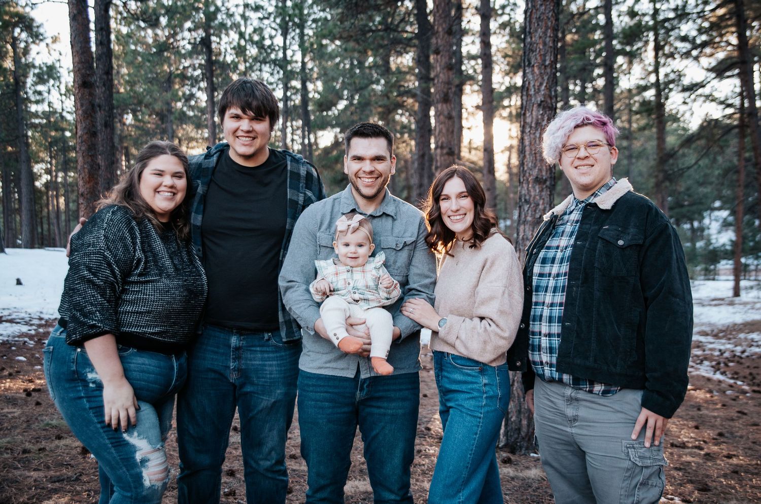 Multiple generations of family members pose together in a wooded outdoor setting.